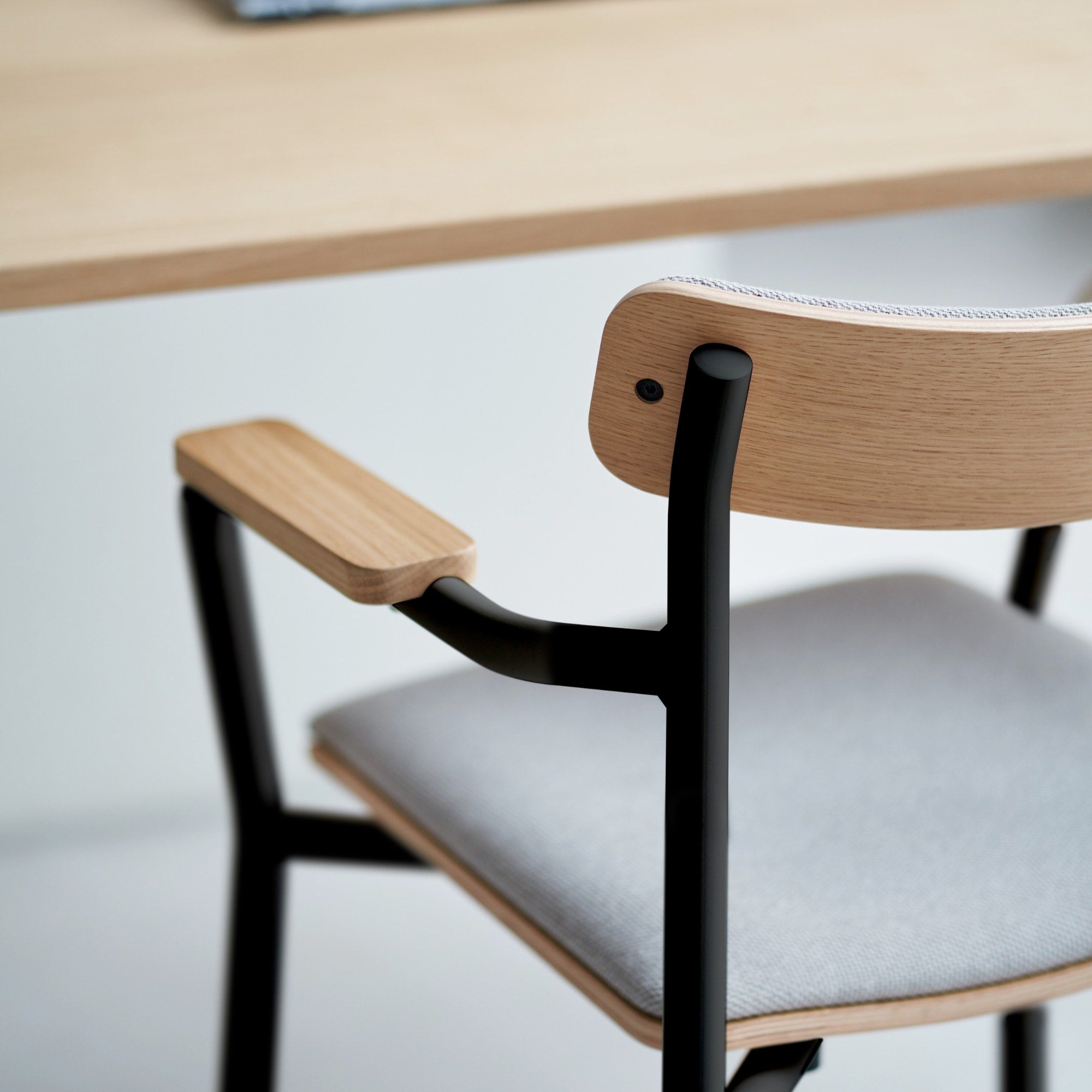 Vue latérale d’une chaise avec assise en tissu, dossier et accoudoirs en bois, piètement en métal noir.