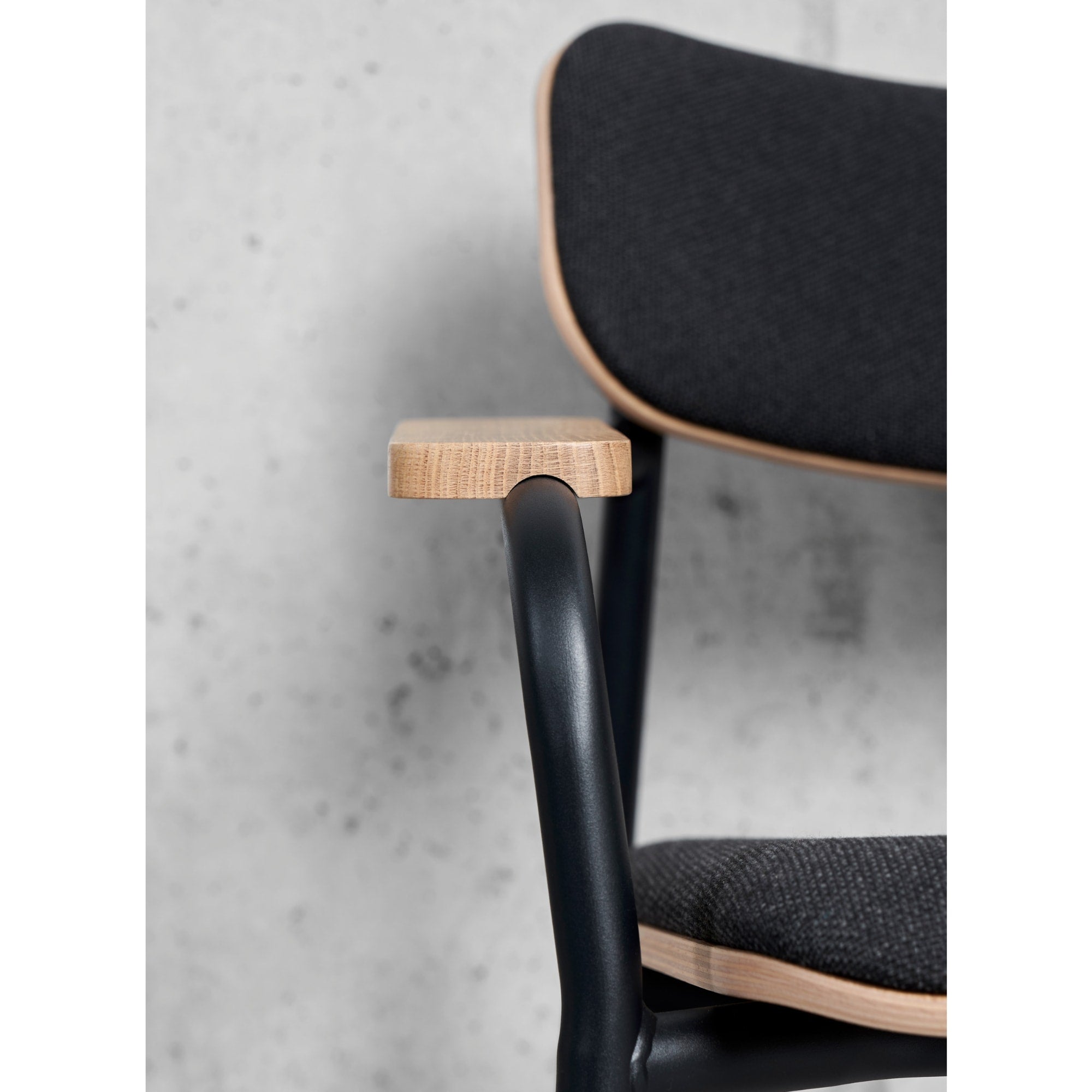Vue proche d’une chaise avec dossier en bois et tissu noir, accoudoirs en bois et structure en métal noir.
