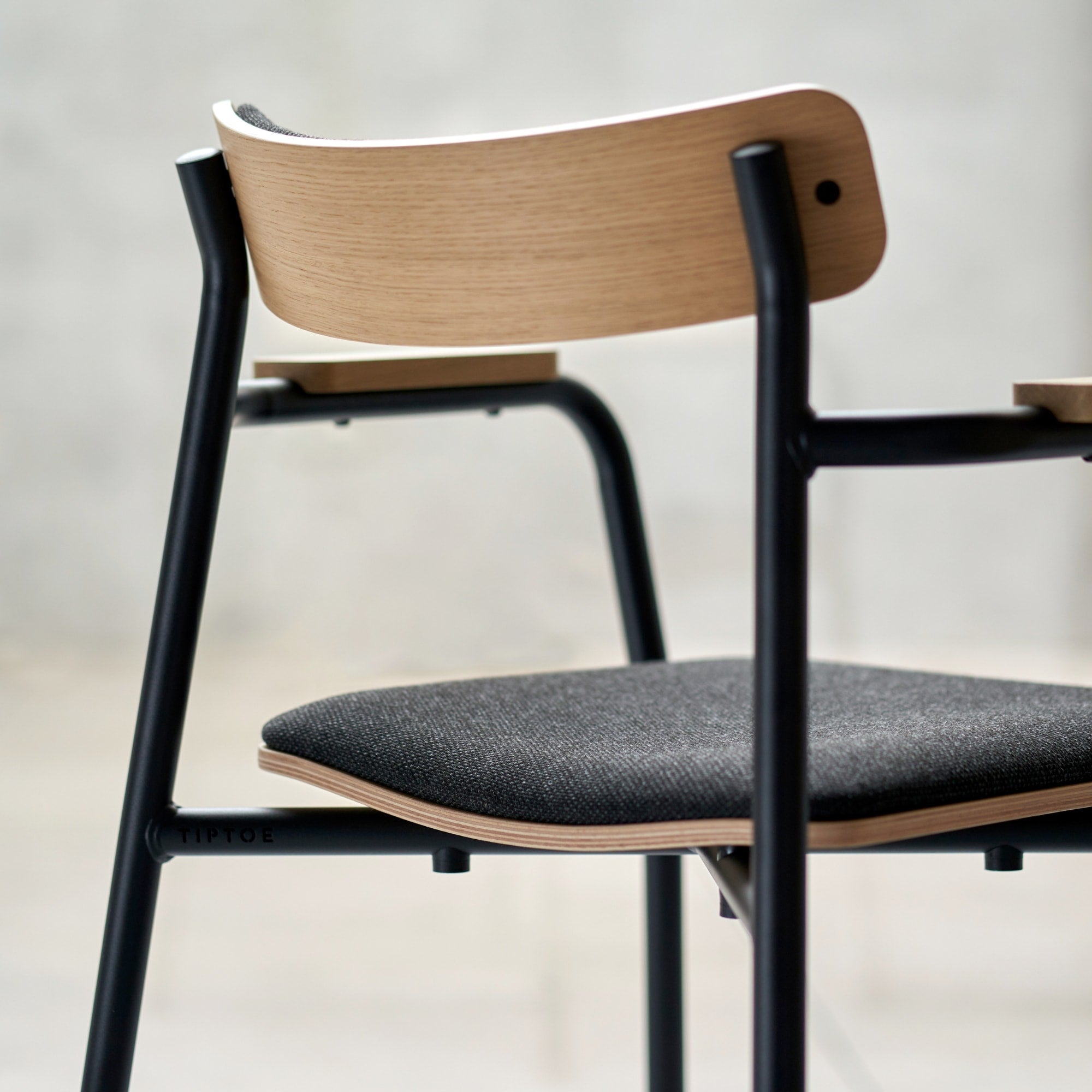 Gros plan sur une chaise avec dossier et assise en bois et tissu, structure métallique et accoudoirs en bois.