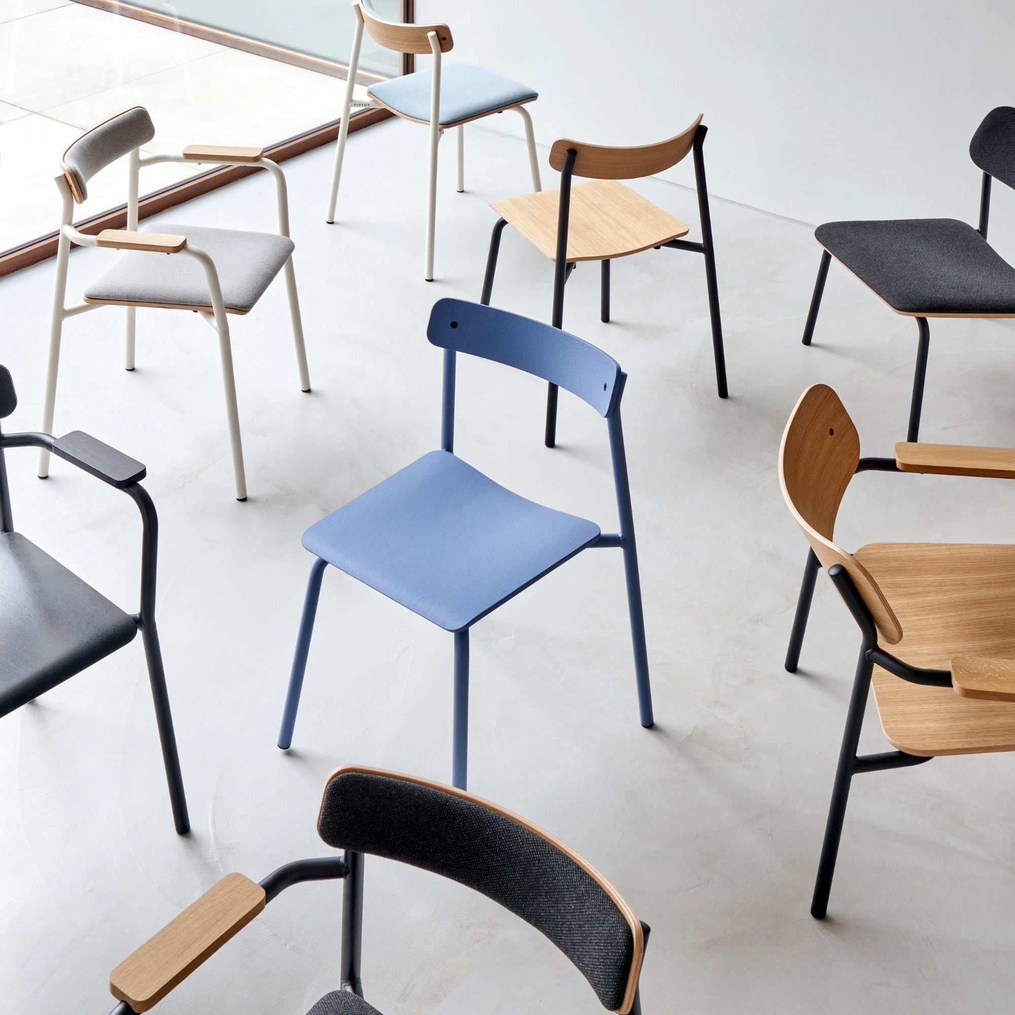 Collection de chaises en bois, tissu et métal dans une salle lumineuse avec grandes fenêtres.