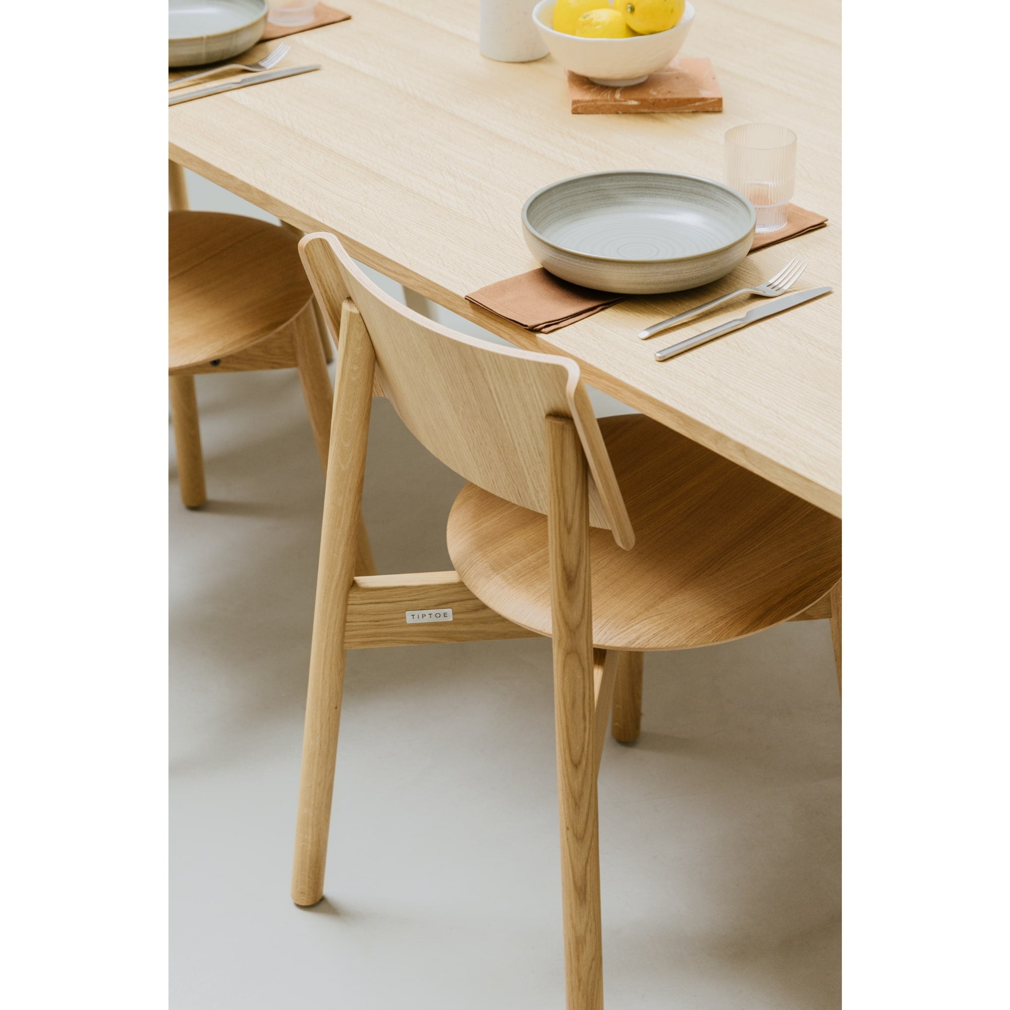 Zoom sur la chaise SSD Full Wood de Tiptoe en chêne naturel, placée autour d’une table assortie, avec une vaisselle minimaliste et des tons clairs soulignant la douceur du bois.