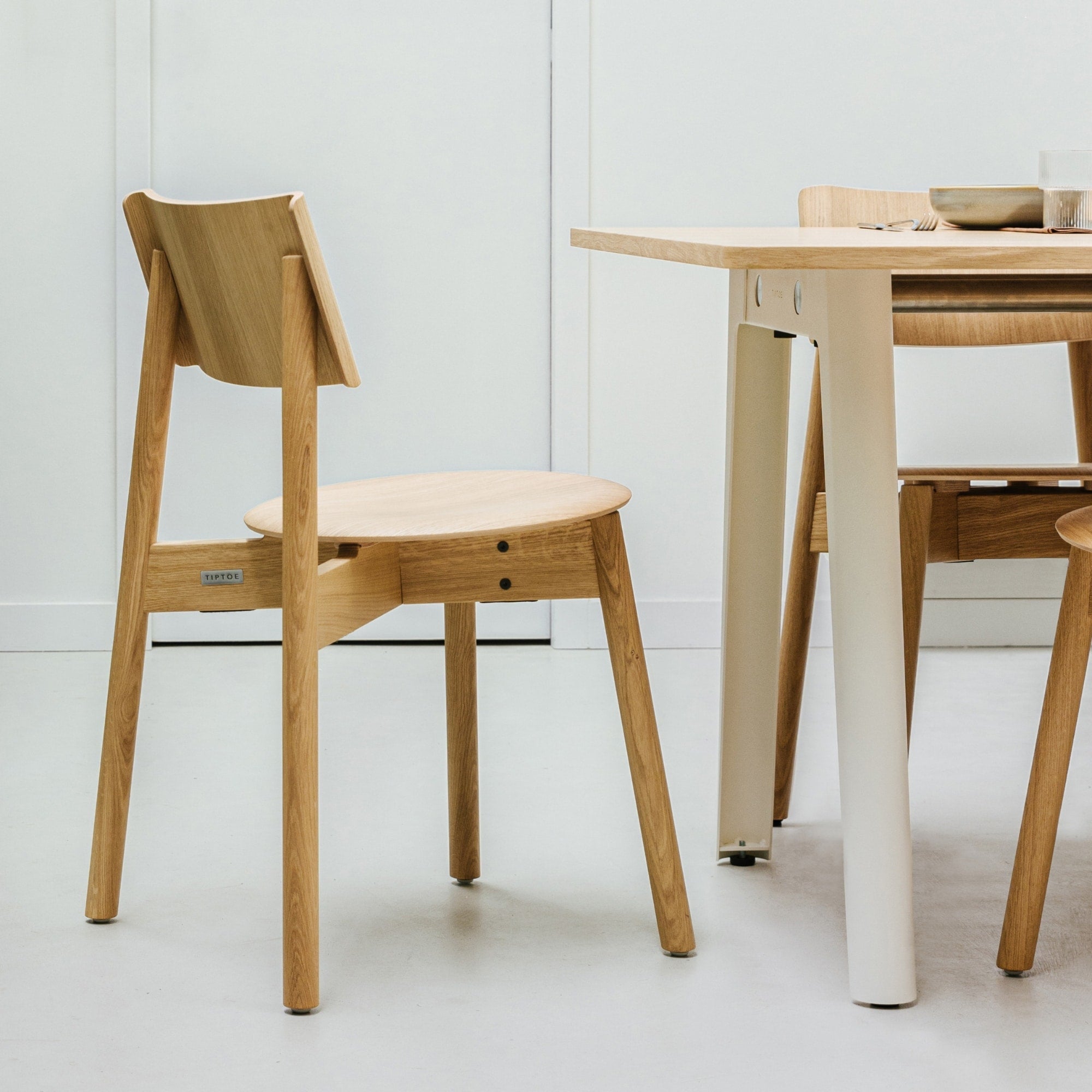 Chaise SSD Full Wood de Tiptoe en chêne naturel, placée près d’une table assortie aux pieds crème, dans un intérieur épuré aux lignes minimalistes.