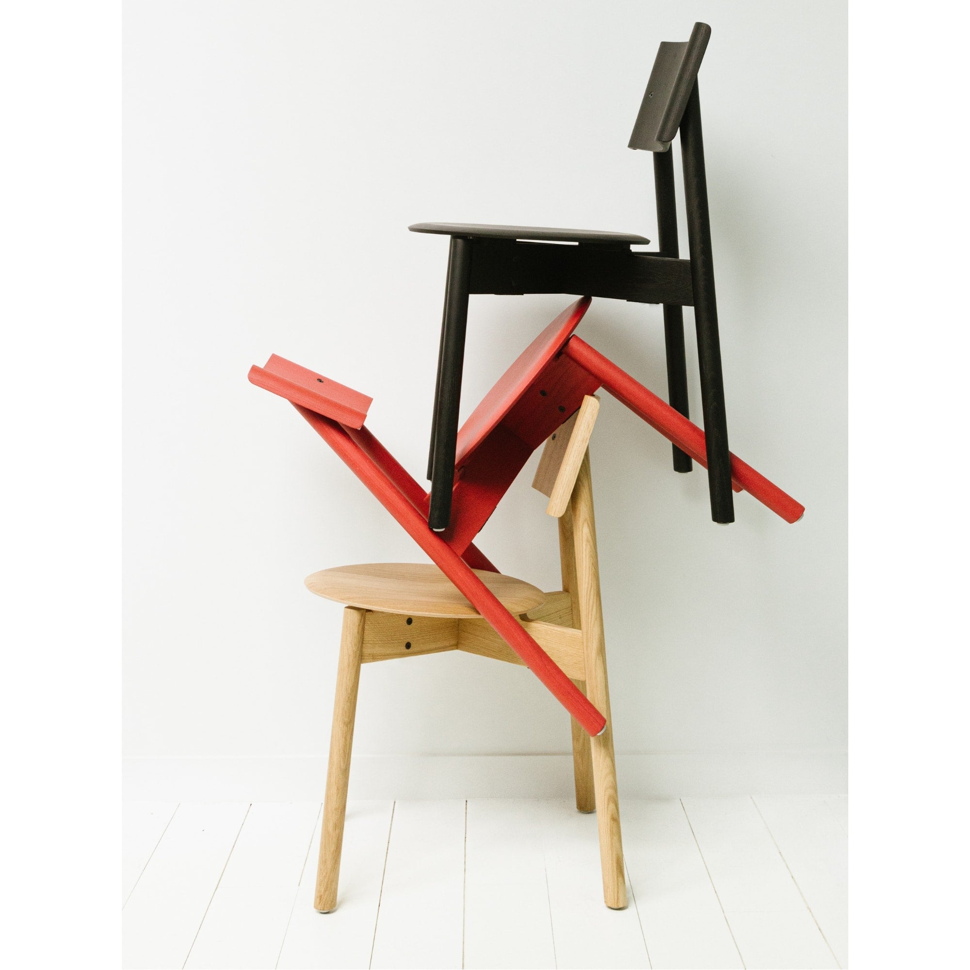 Empilement sculptural de trois chaises SSD Full Wood de Tiptoe en chêne naturel, rouge et noir, formant une composition graphique sur fond blanc.