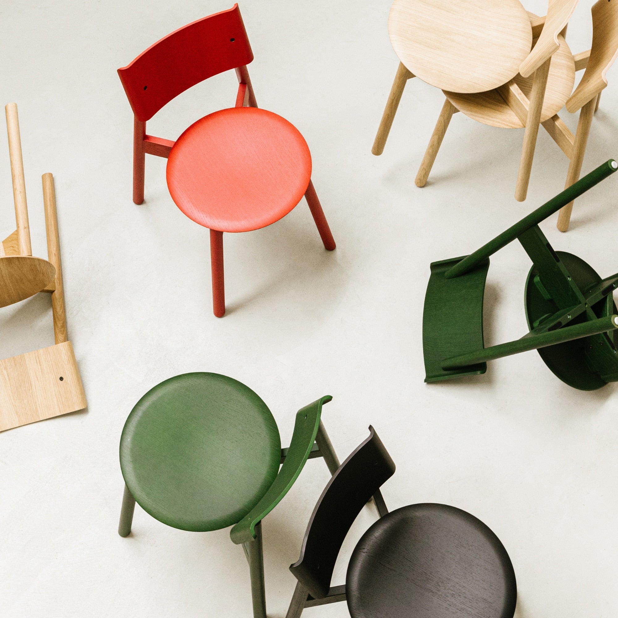 Vue du dessus de plusieurs chaises SSD Full Wood de Tiptoe en chêne teinté noir, vert, rouge et naturel, dispersées au sol pour mettre en valeur la diversité des coloris et l’esthétique du design.