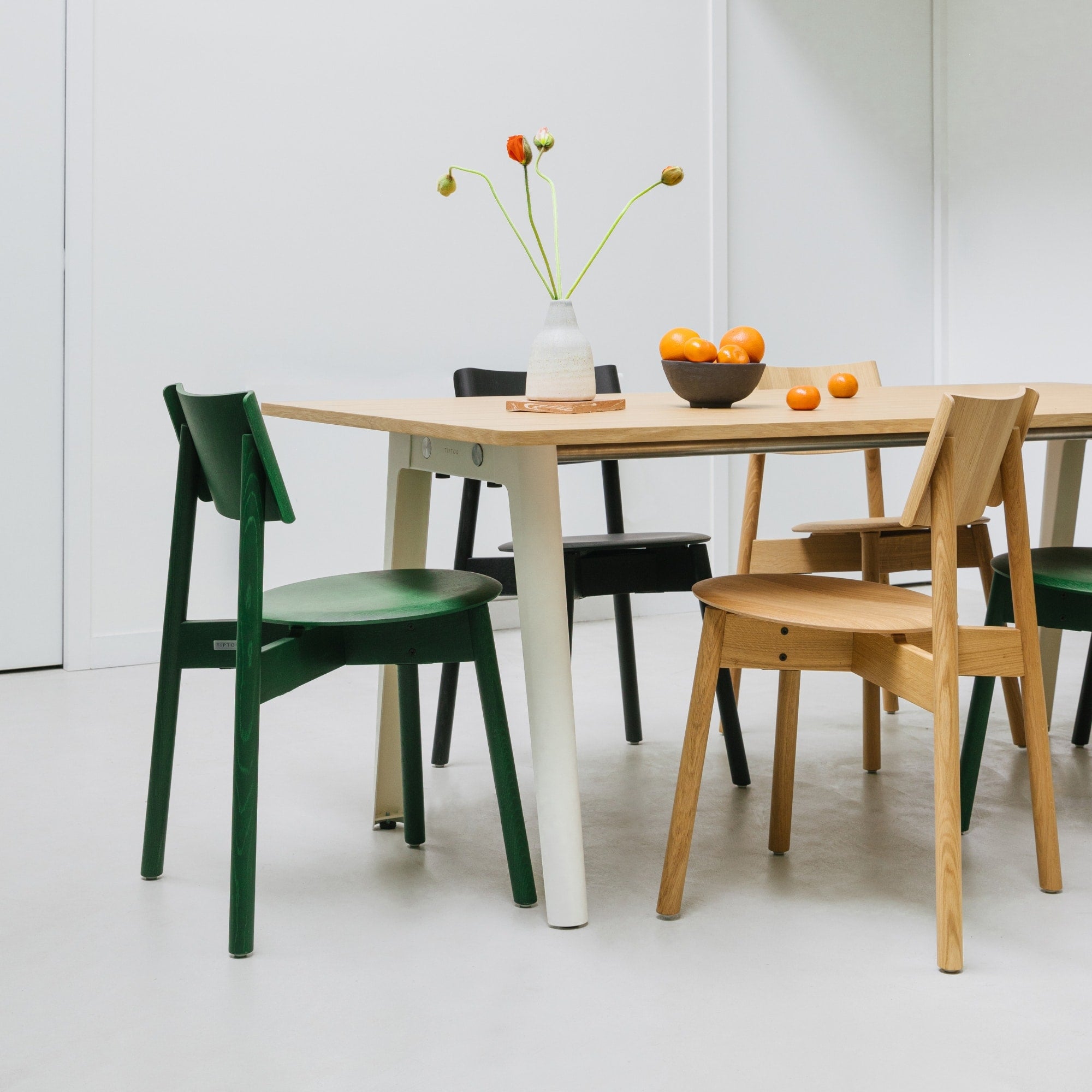 Chaises SSD Full Wood de Tiptoe en chêne naturel, noir et vert, disposées autour d’une table en bois clair aux pieds crème, dans un intérieur minimaliste et lumineux.