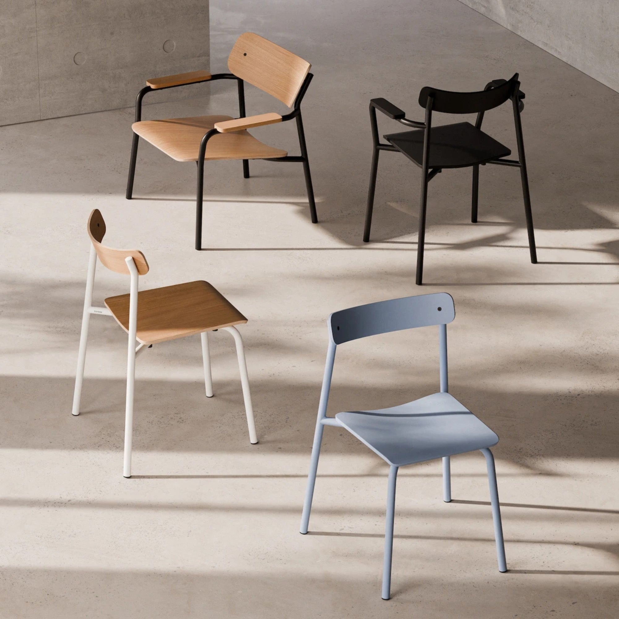 Fauteuils et chaises Tiptoe en bois et métal aux finitions variées, présentés dans une lumière naturelle sur sol en béton brut.