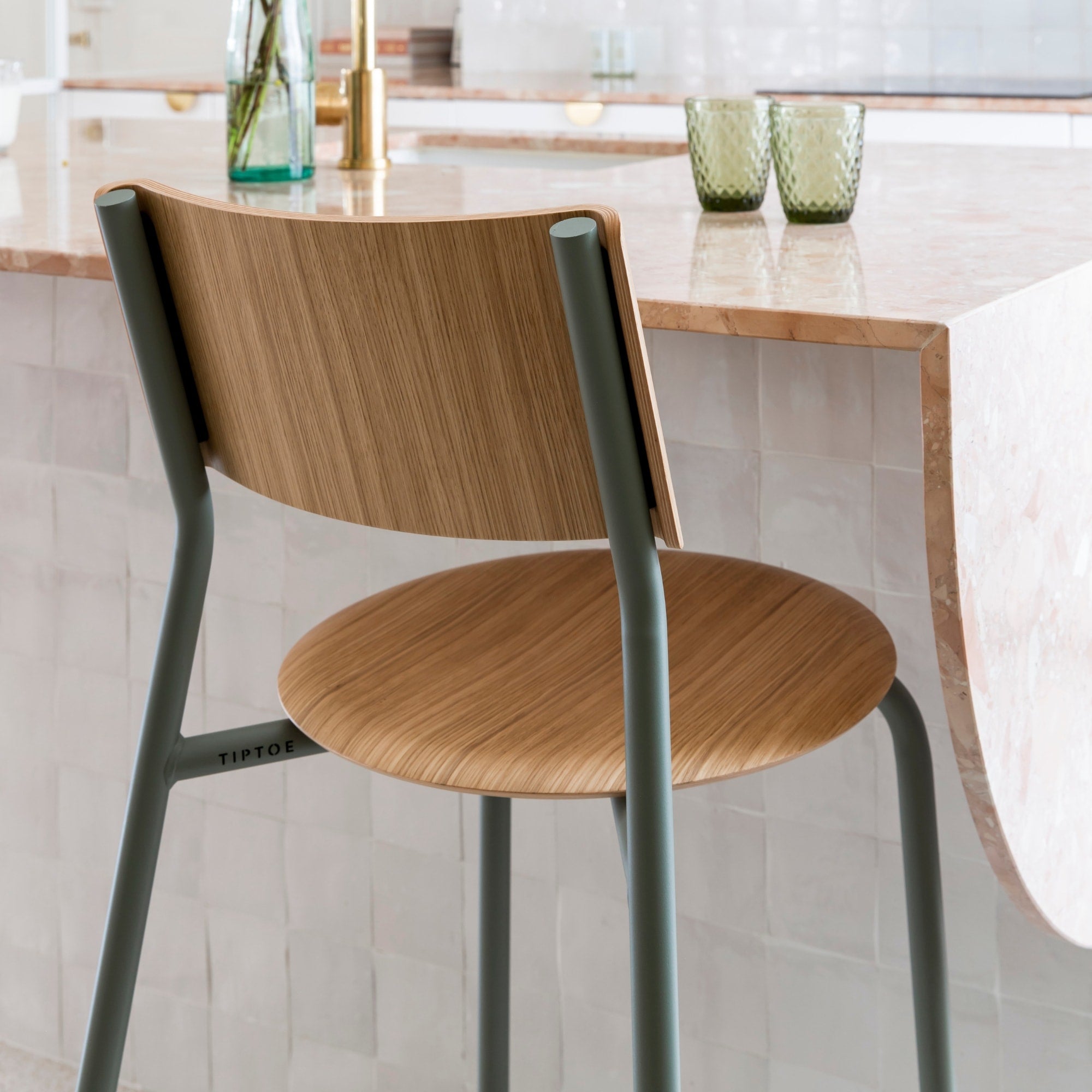 Gros plan sur l’assise et le dossier d’une chaise haute en bois clair avec structure métallique gris eucalyptus devant un comptoir en marbre clair.