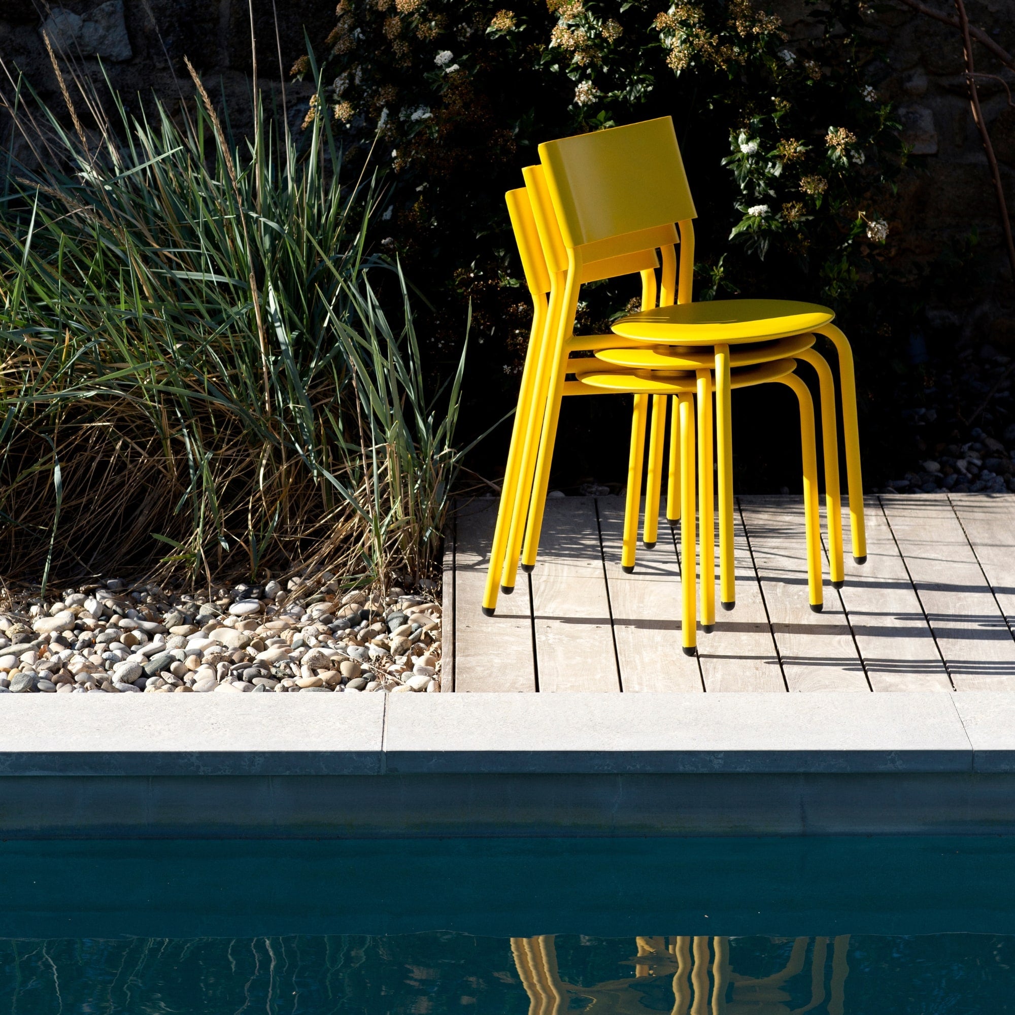 Chaises empilées en métal et plastique recyclé jaune Tiptoe, posées sur une terrasse en bois au bord d’une piscine.
