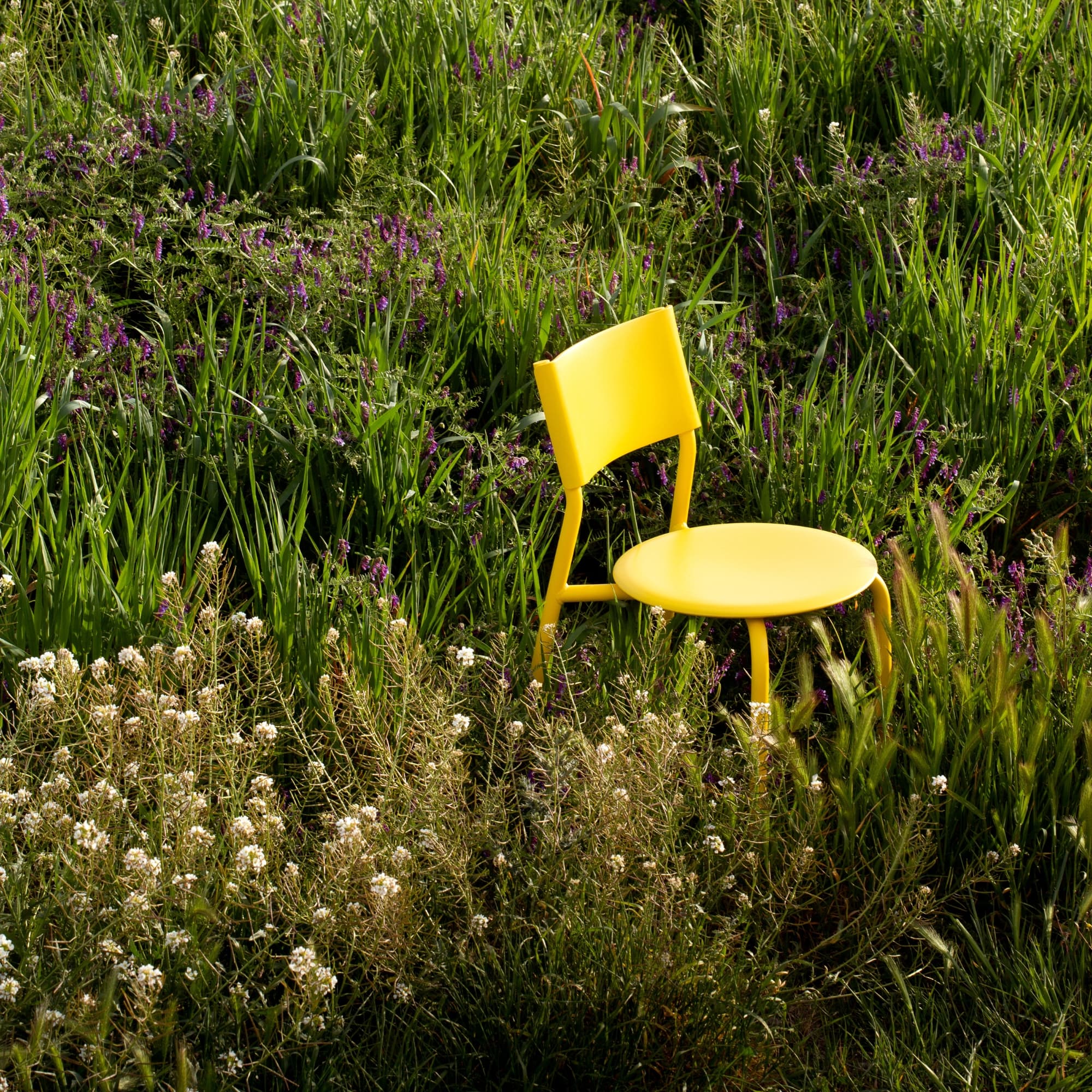 Chaise en métal et plastique recyclé jaune Tiptoe posée au milieu d’une prairie verdoyante, entourée de fleurs sauvages.