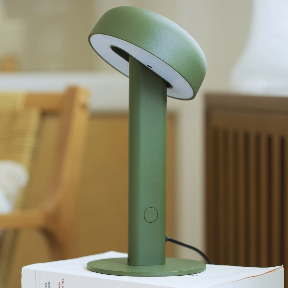 Gros plan sur la lampe de table Nod en métal vert, posée sur un livre posé sur un bureau.