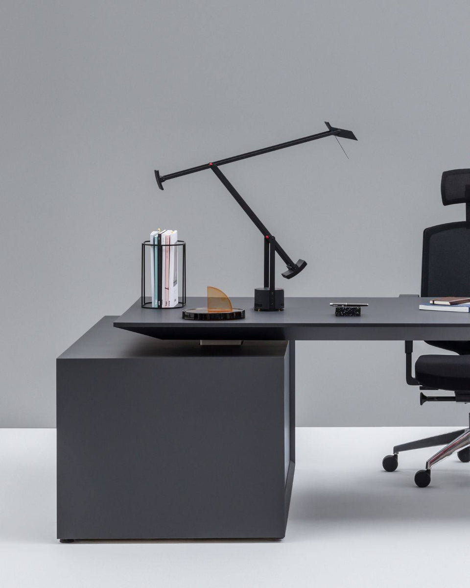 Lampe de bureau design à éclairage indirect sur bureau professionnel noir, avec fauteuil ergonomique et accessoires de travail.