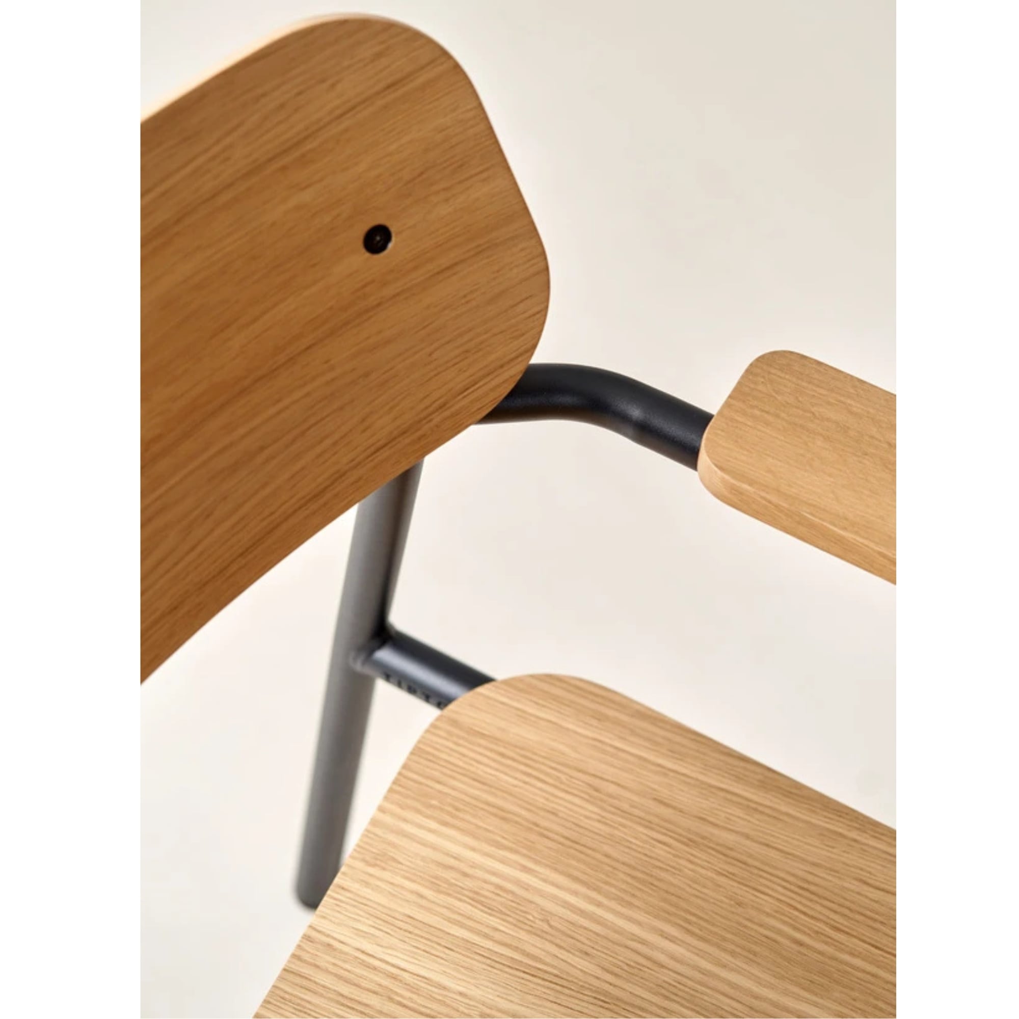 Zoom sur les détails du fauteuil d’étude avec dossier, assise et accoudoir en bois clair, structure tubulaire noire, sur fond beige.