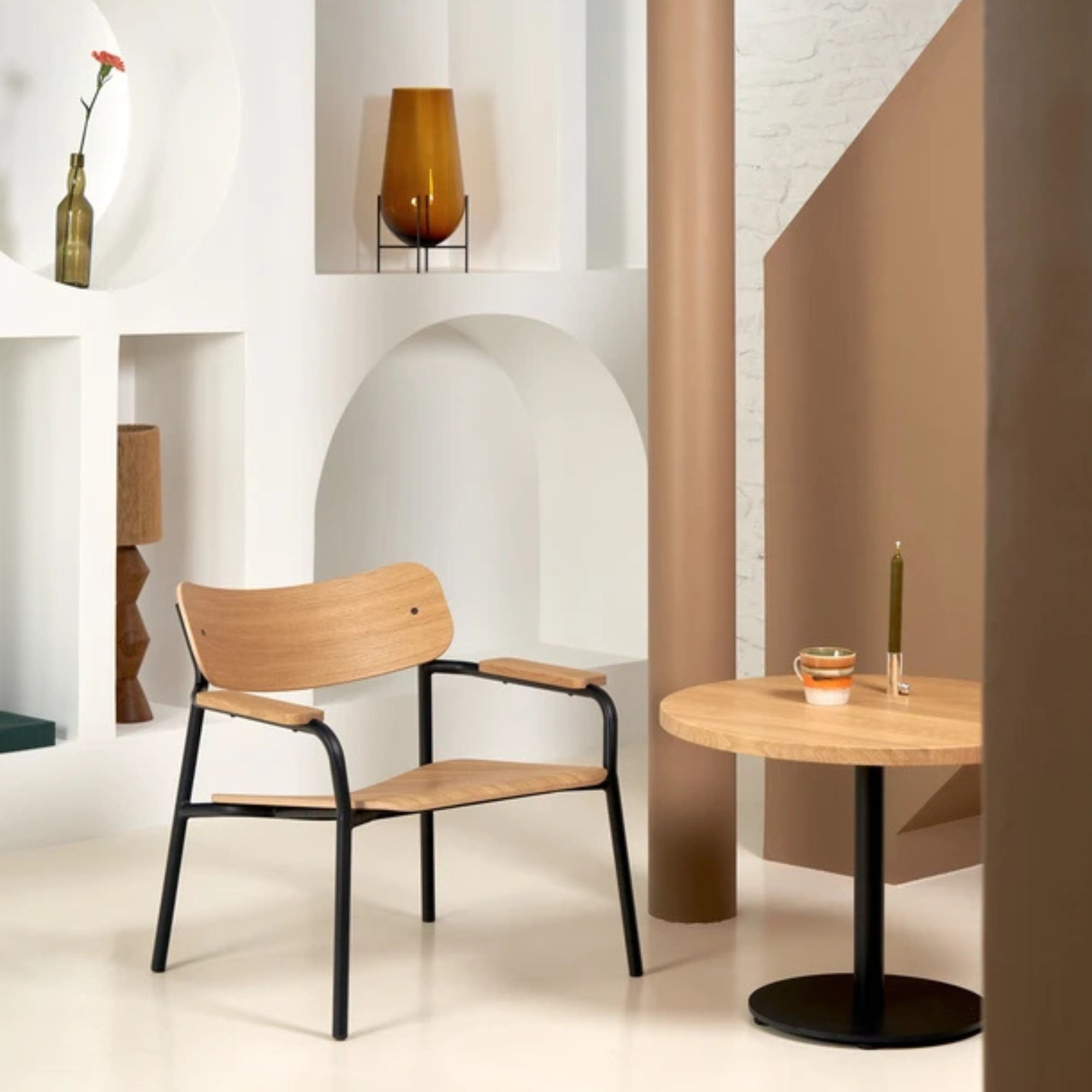 Fauteuil Etude en bois clair et structure noire, placé à côté d’une table ronde assortie dans un intérieur contemporain aux tons beiges et blancs.