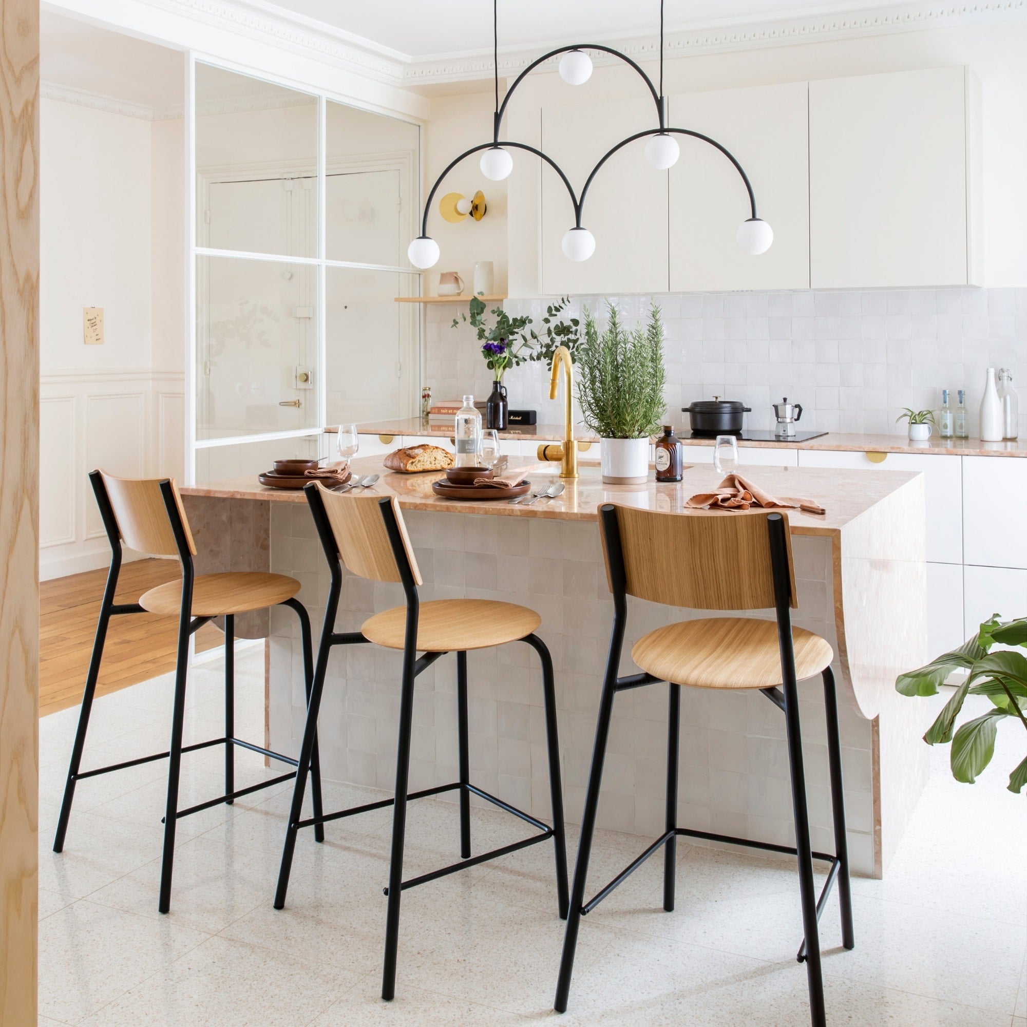 Trois chaises hautes en bois clair avec piètement métallique noir autour d’un îlot central en marbre clair dans une cuisine moderne.