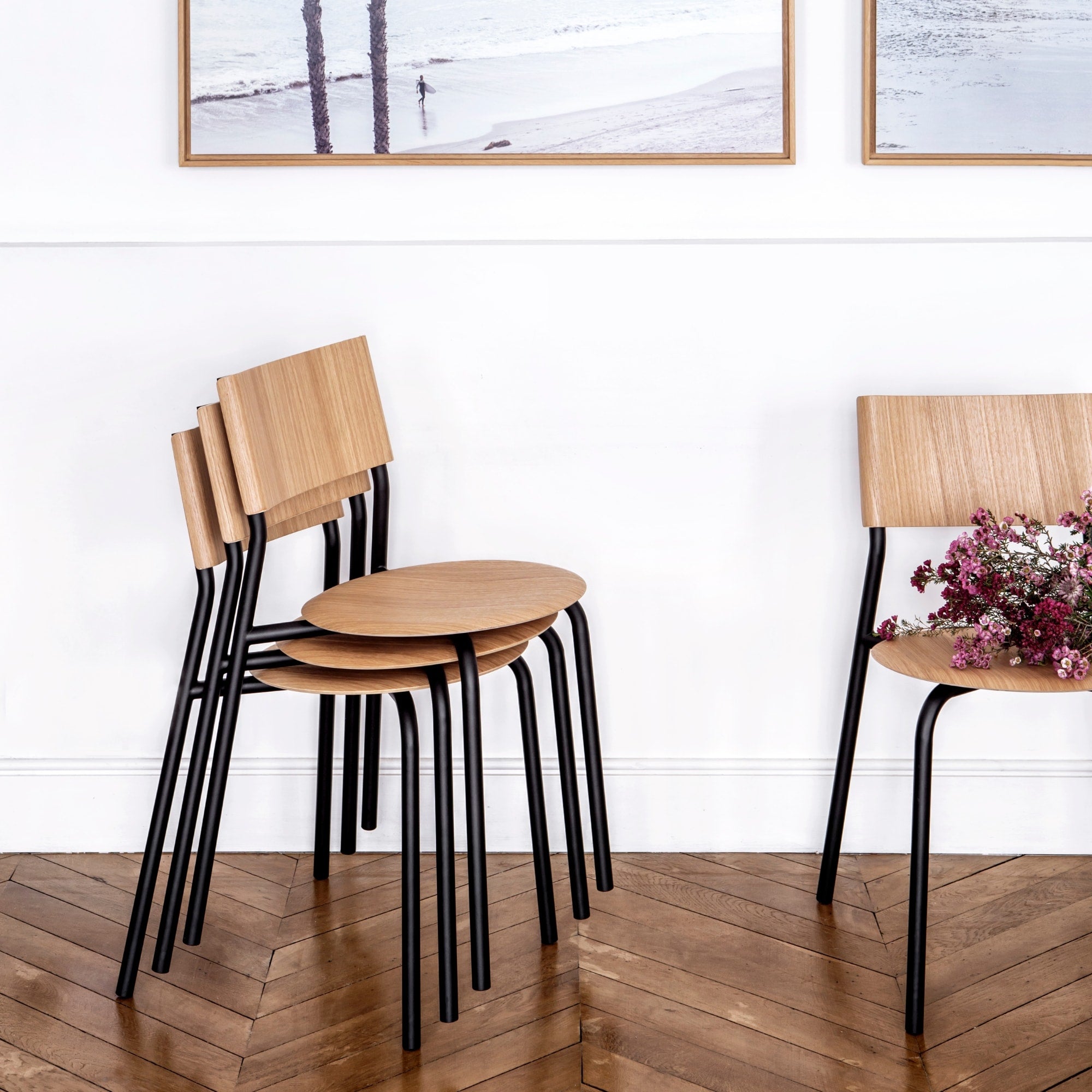 Chaises empilées, en bois et acier, modèle SSD de la marque Tiptoe, couleur noire, avec un design moderne et épuré, posées sur un sol en parquet.