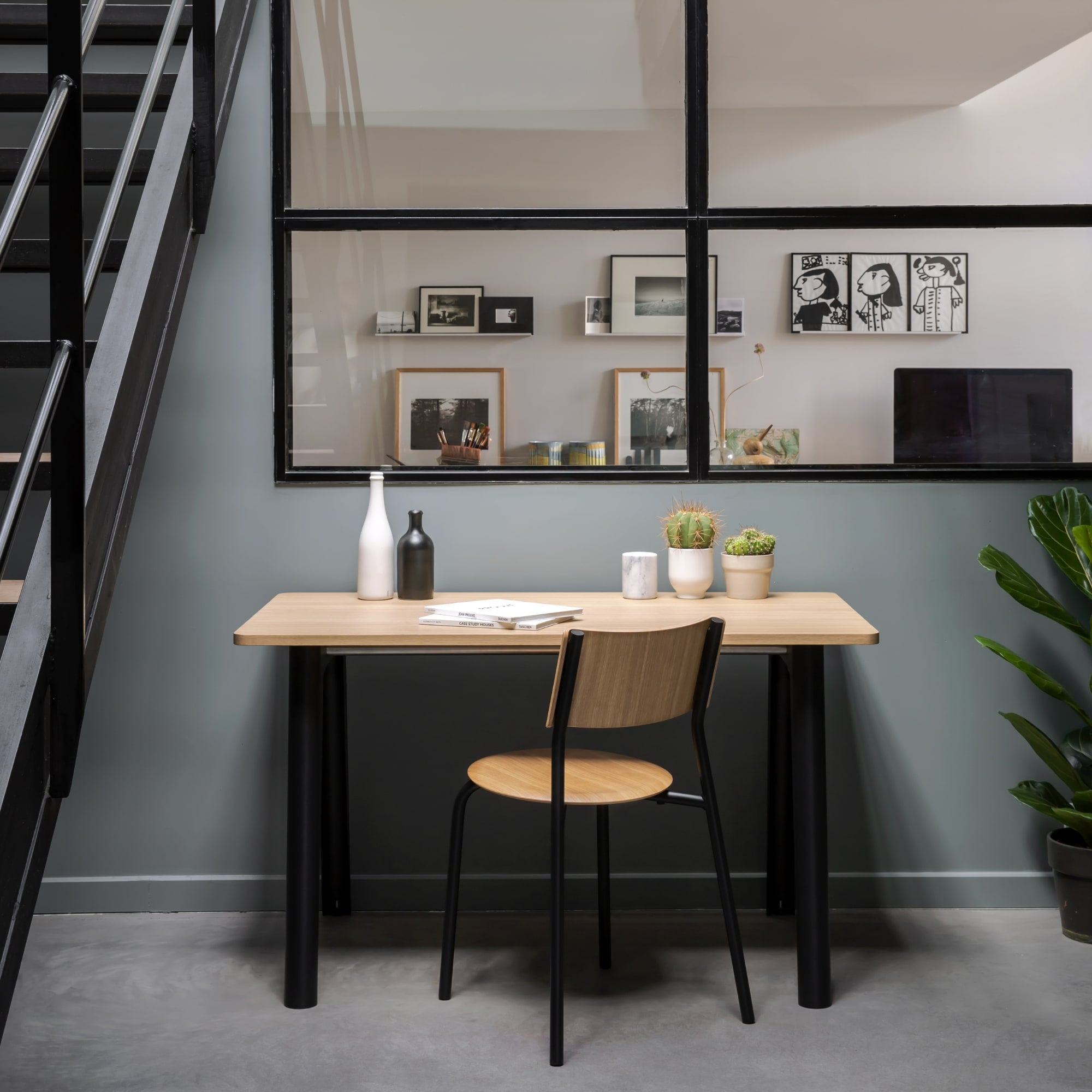 Chaise en bois et acier, modèle SSD de Tiptoe, couleur noire, placée autour d’une table en bois avec des plantes en pot, un vase et des objets décoratifs sur un sol béton dans un environnement moderne.