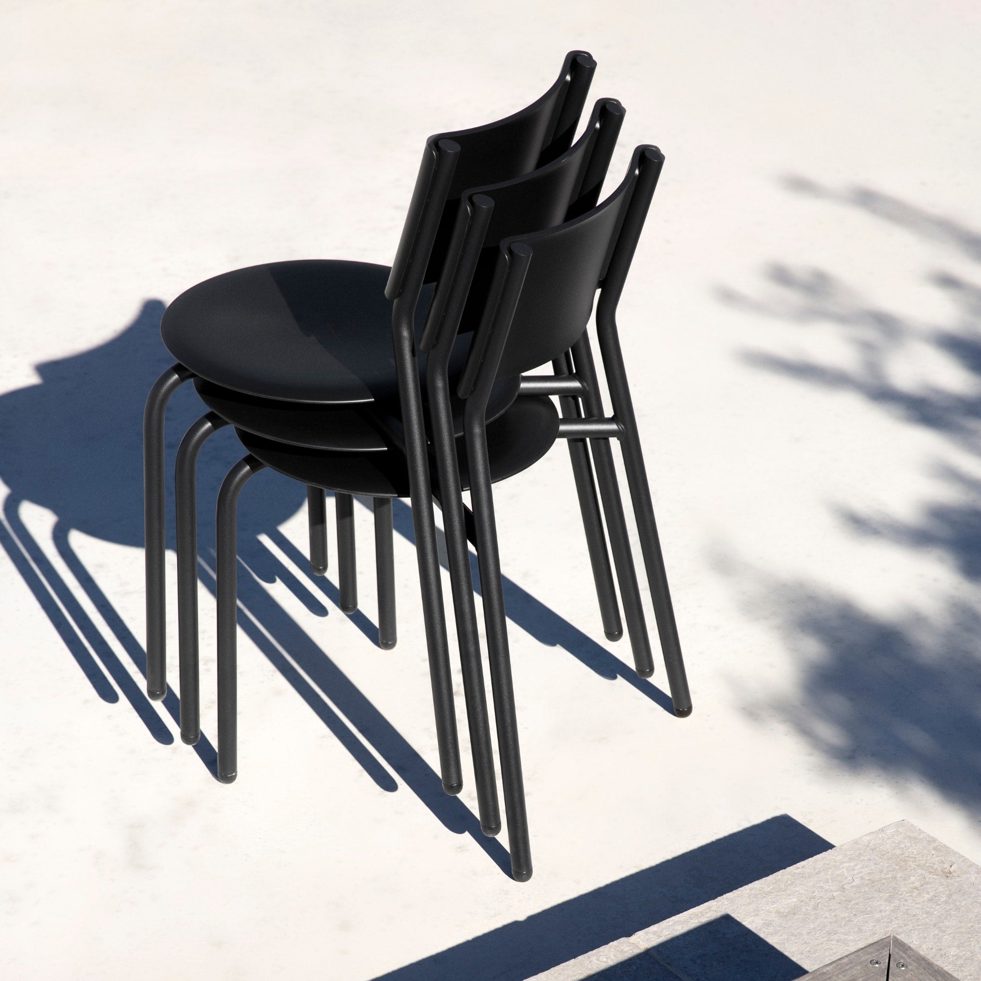 Trois chaises de jardin en métal et plastique recyclé noir empilées, finition mate et silhouette épurée.