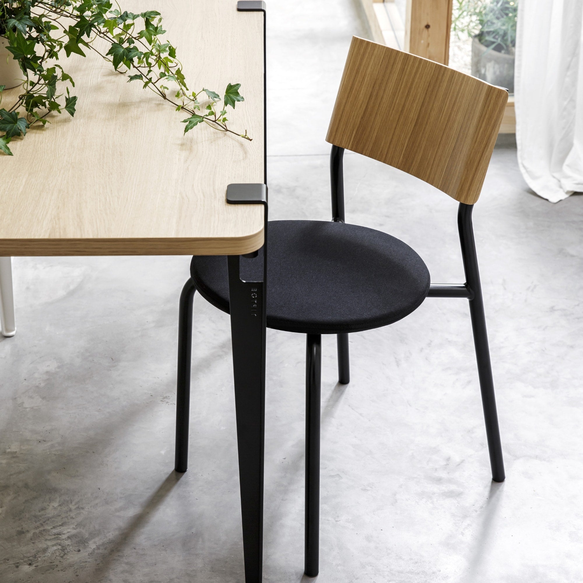 Chaise SSD Soft de Tiptoe avec piètement noir, dossier en bois clair et assise en tissu noir, placée à côté d’une table en bois clair dans un espace lumineux.