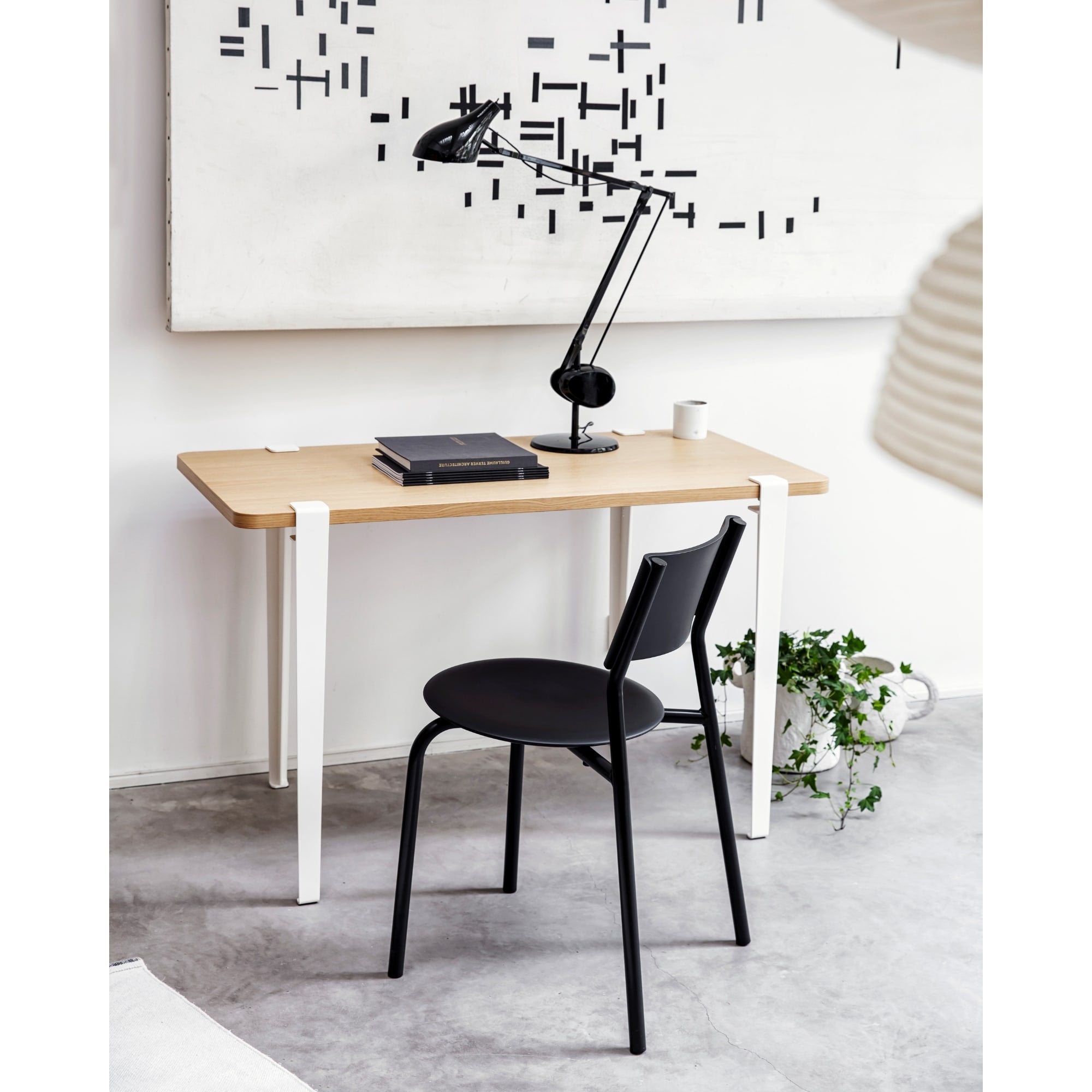 Chaise noire en plastique recyclé de Tiptoe devant une table en bois avec une lampe de bureau et des objets décoratifs.