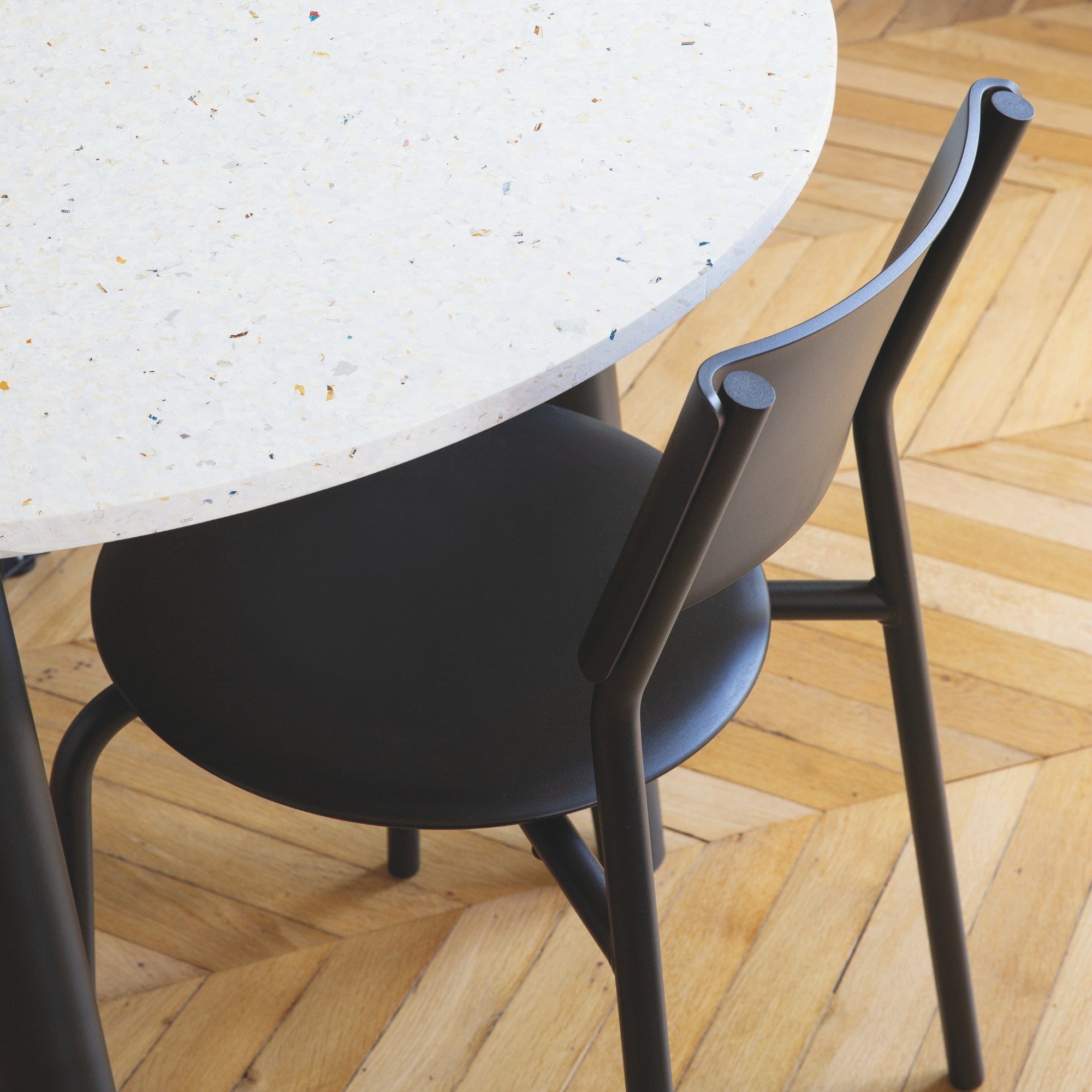 Chaise noire en plastique recyclé, placée à côté d’une table au dessus d’un sol en parquet, avec un plateau en terrazzo aux couleurs naturelles.