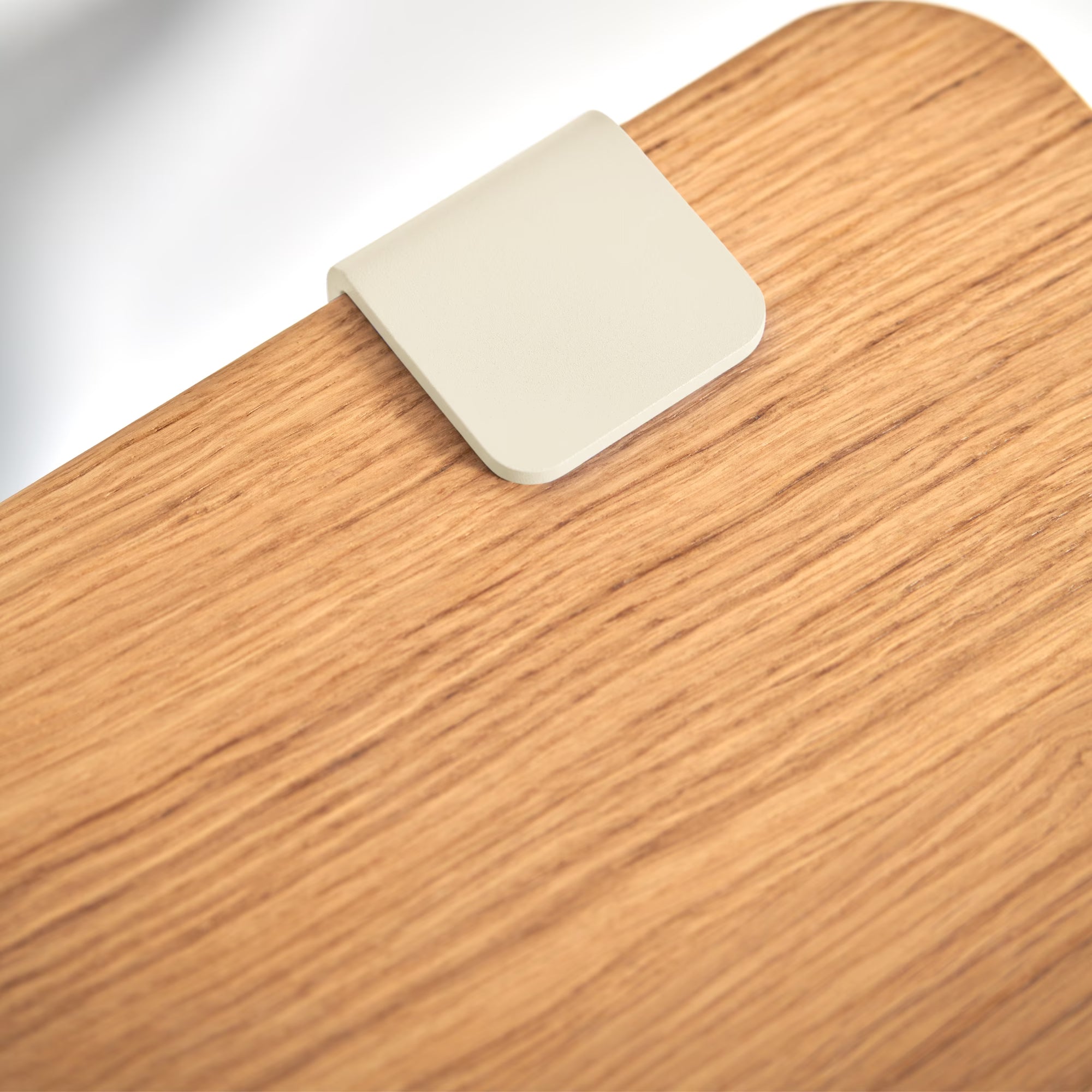 Gros plan sur pièce métallique blanc crème fixée au plateau bois, détail net sur veinage et contraste matière.