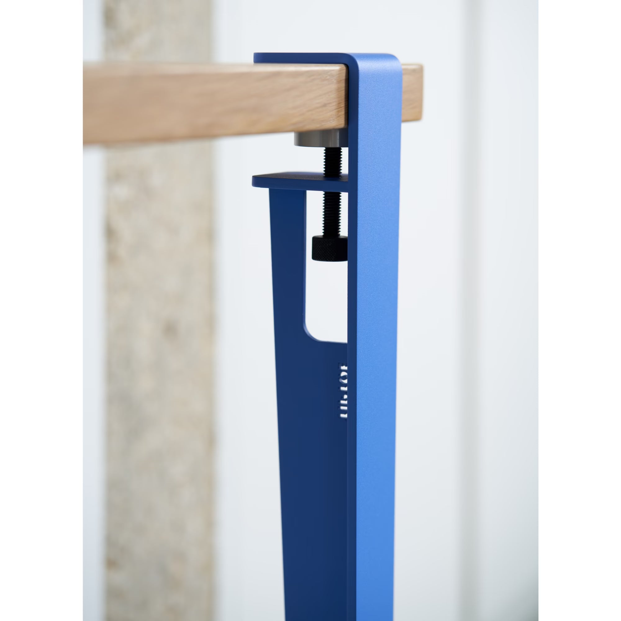 Gros plan sur patte de fixation en métal bleu azur serrant un plateau en bois clair, vis et boulon réglables.