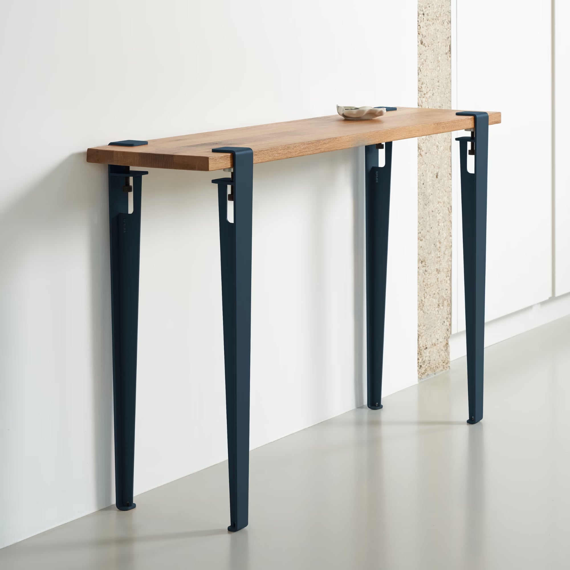 Console en bois massif avec pieds en métal bleu nuit, design épuré et élégant contre un mur blanc.