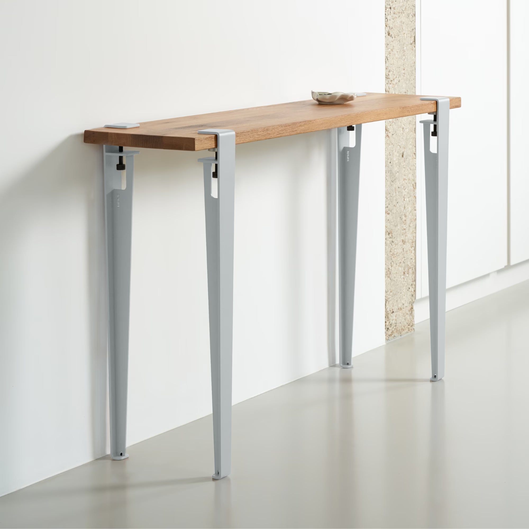 Console en bois massif avec pieds en métal bleu pâle, installée contre un mur blanc, vue en perspective sur sol lisse.