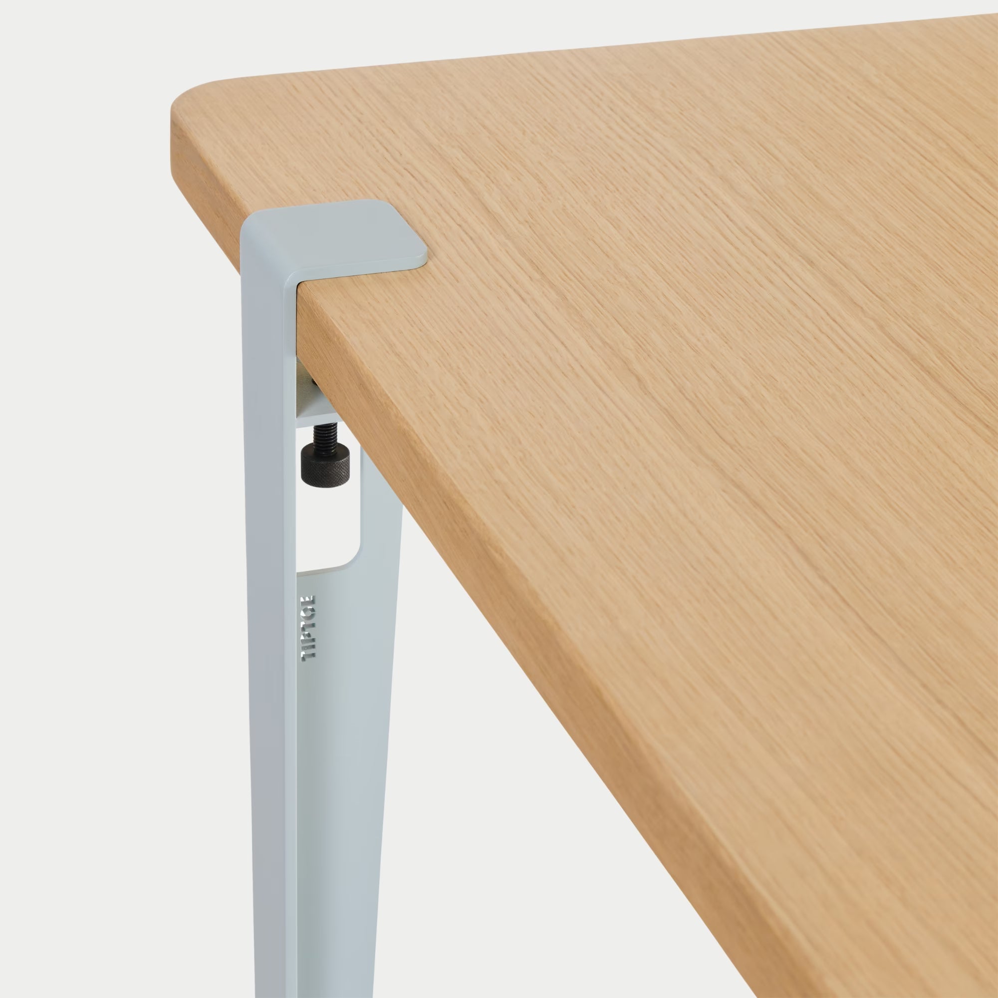 Vue rapprochée : plateau bois clair et fixation métal bleu pâle, détail de l’assemblage sur fond blanc.