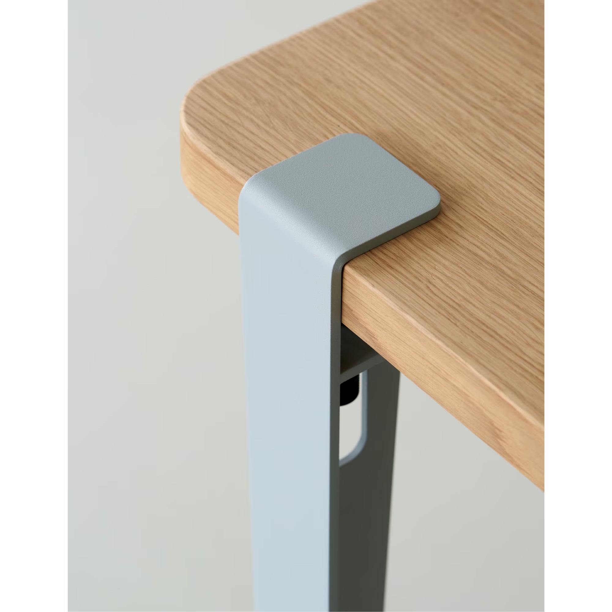 Gros plan sur angle de plateau en bois clair et bride de fixation en métal bleu pâle, vis apparente, fond neutre.