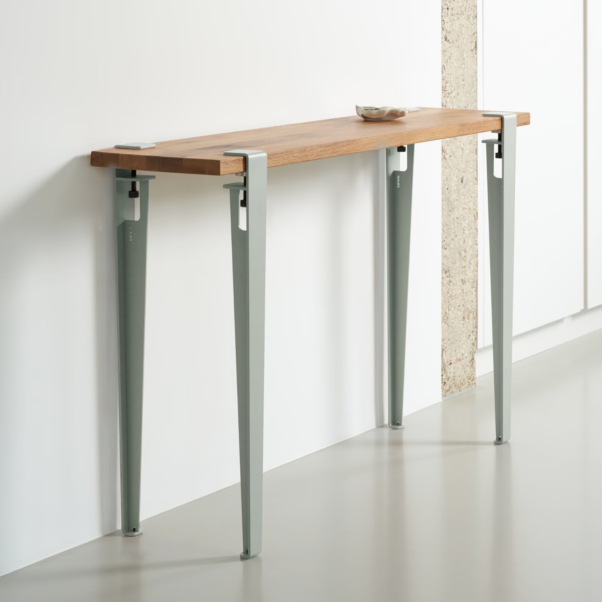 Console étroite avec plateau bois massif et pieds métal gris eucalyptus, installée contre un mur clair, vue en perspective.