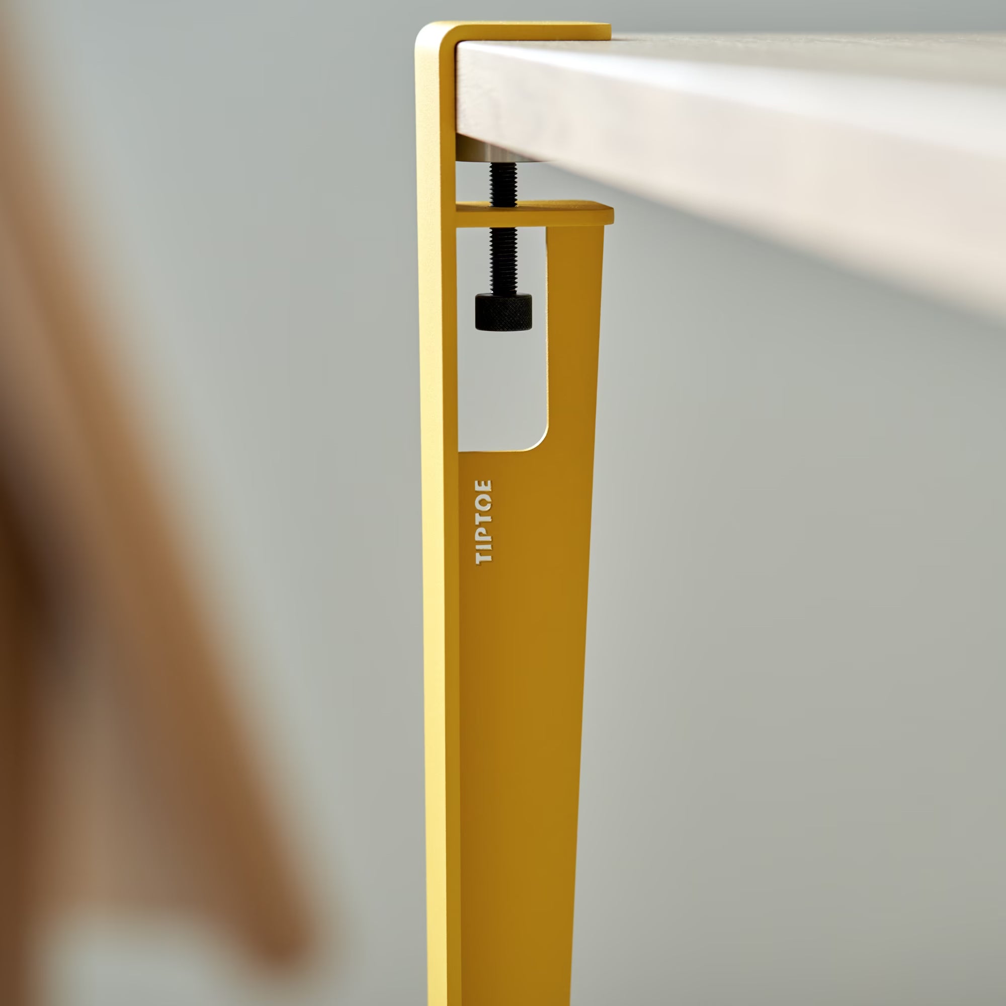 Fixation métallique jaune brioche avec inscription Tiptoe, solidement vissée sous un plateau en bois clair