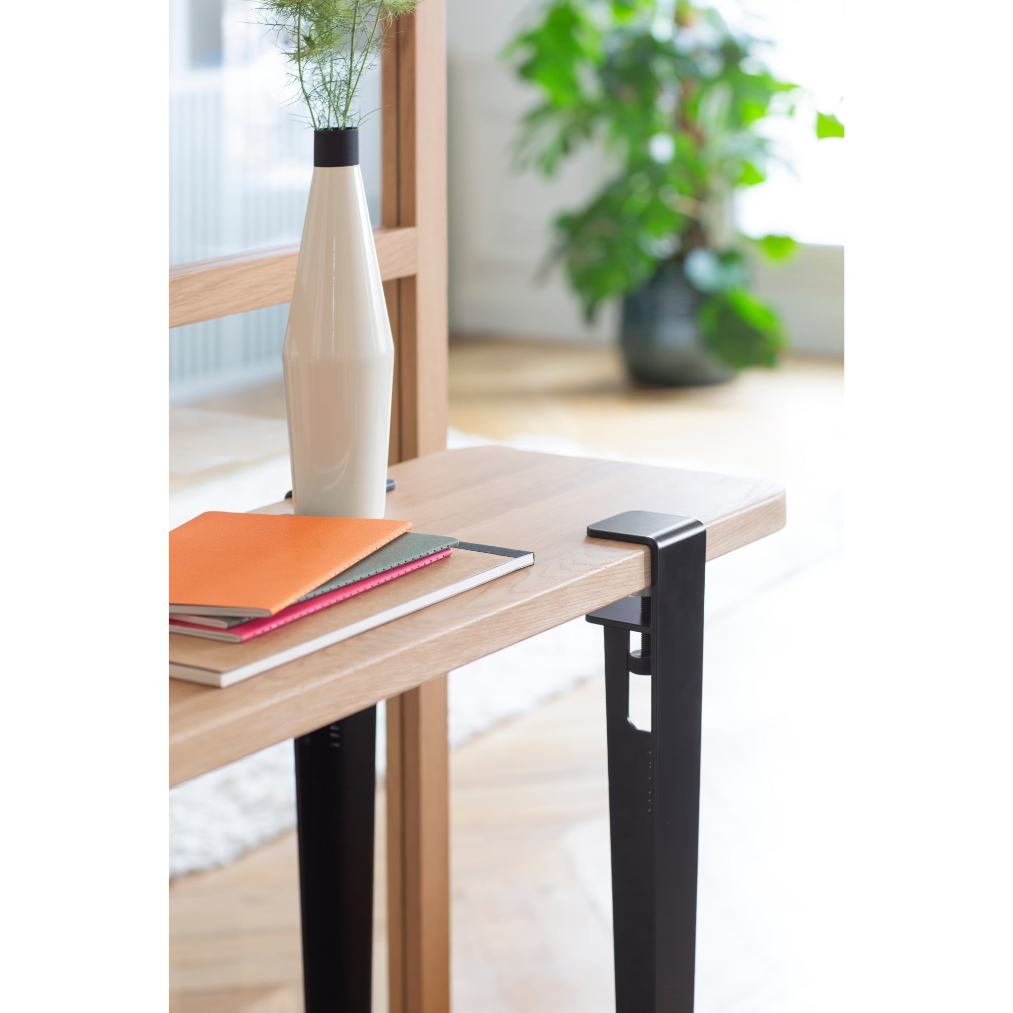 Console en bois et métal noir, plateau décoré d’un vase blanc et de carnets colorés, ambiance lumineuse près d’une verrière.