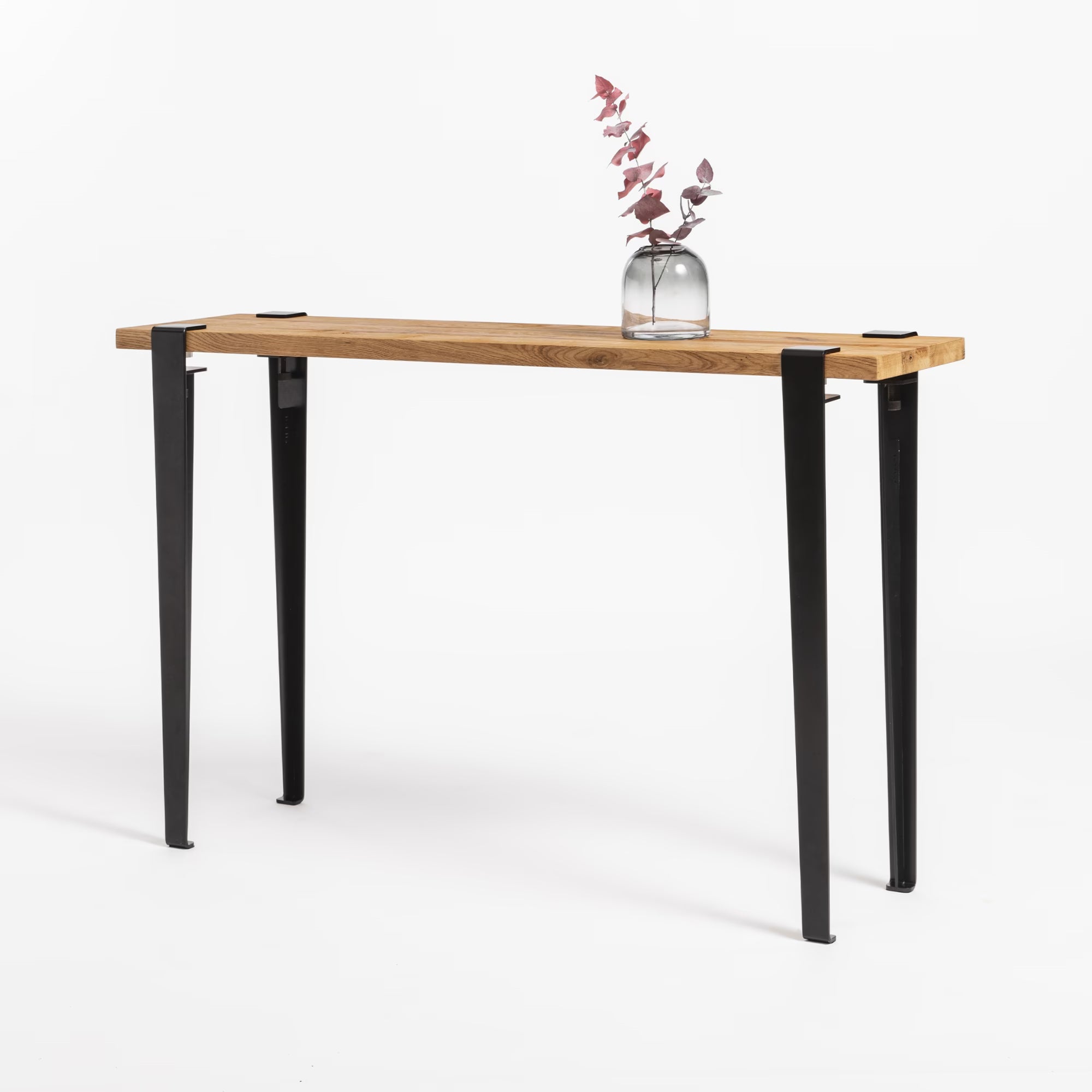 Petite console en bois et métal noir, plateau chêne clair, décorée d’un vase posé sur fond neutre.