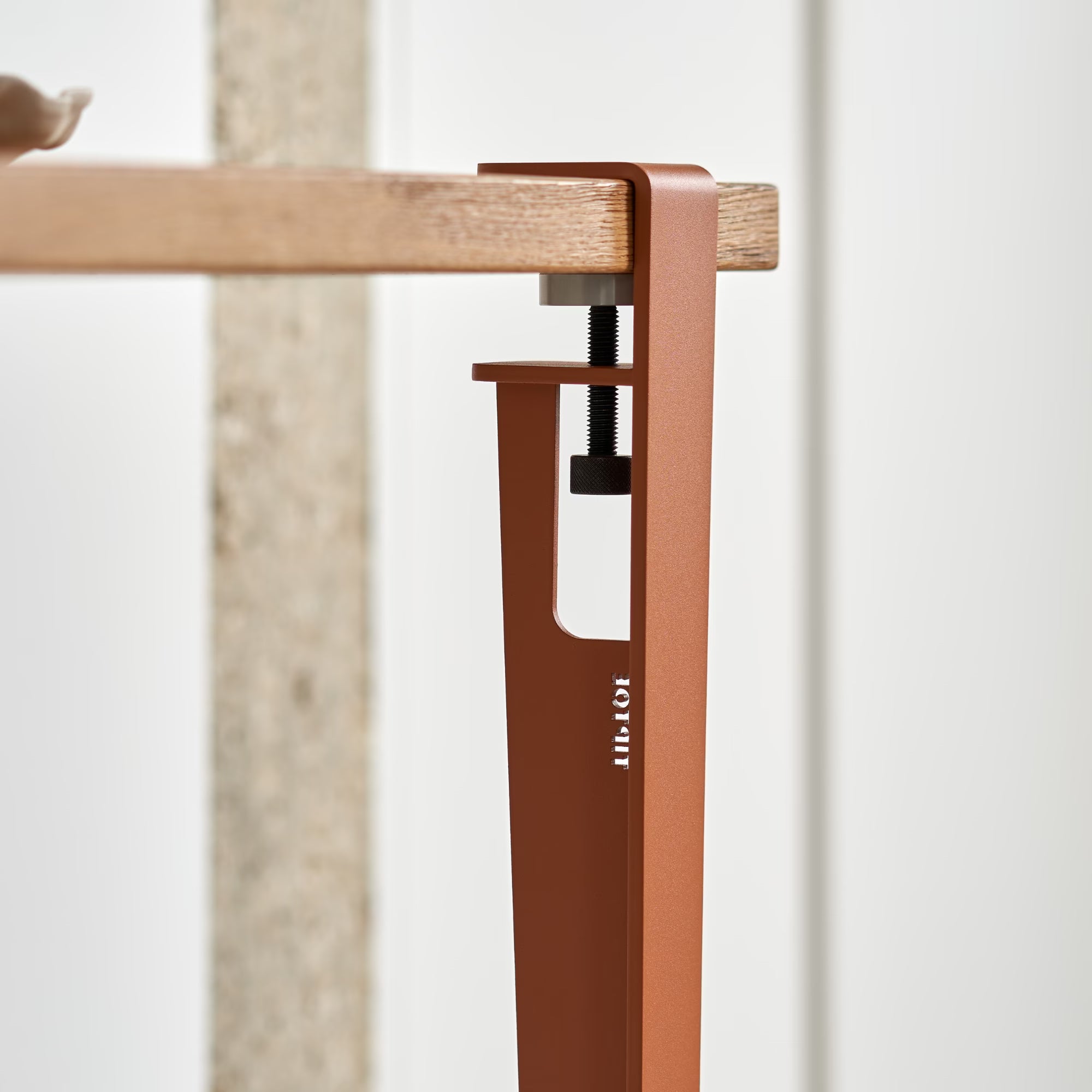 Fixation métallique rouge tangerine avec inscription Tiptoe, solidement vissée sous un plateau en bois clair