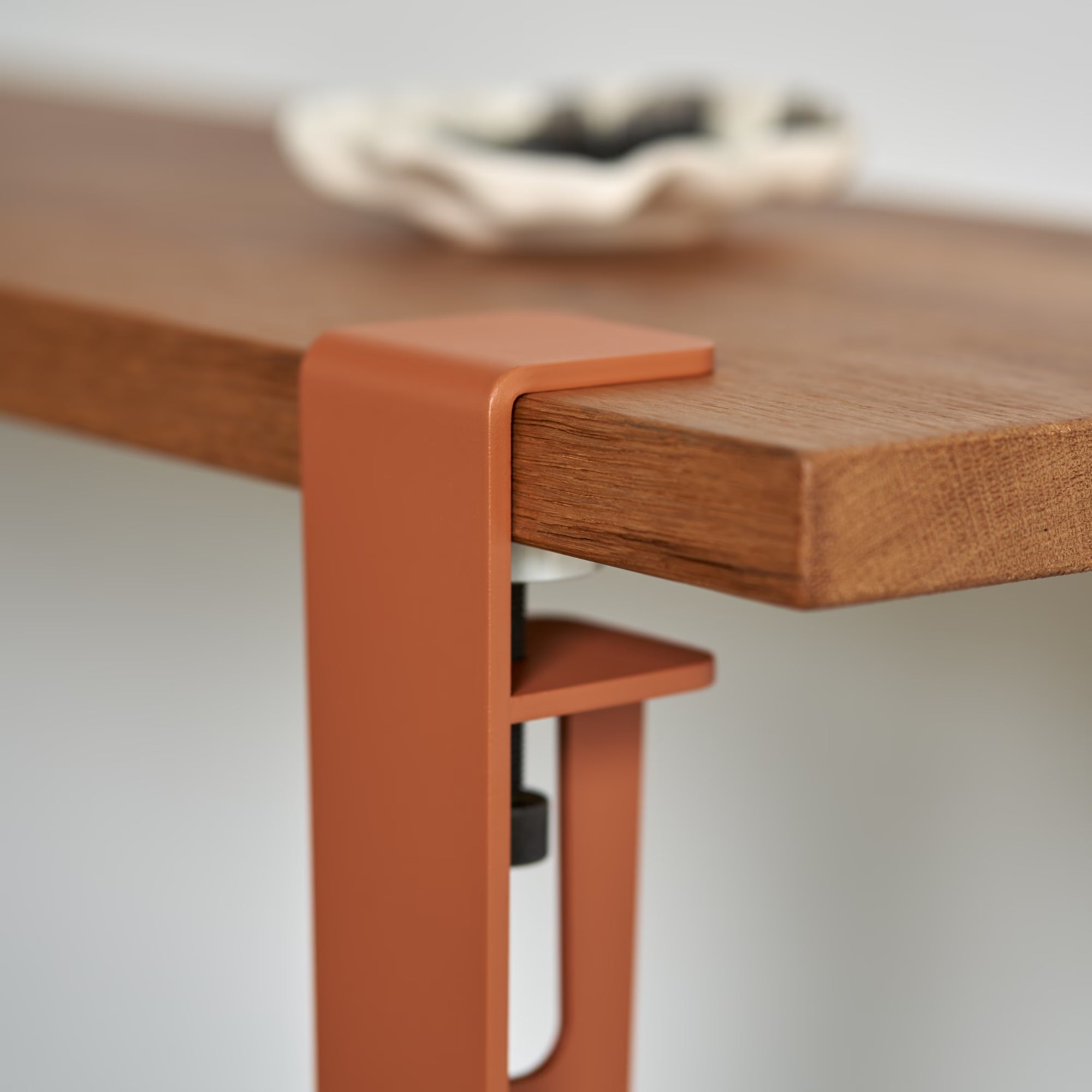 Vue rapprochée d’un plateau en bois massif avec patte de fixation en métal rouge tangerine, console Tiptoe.