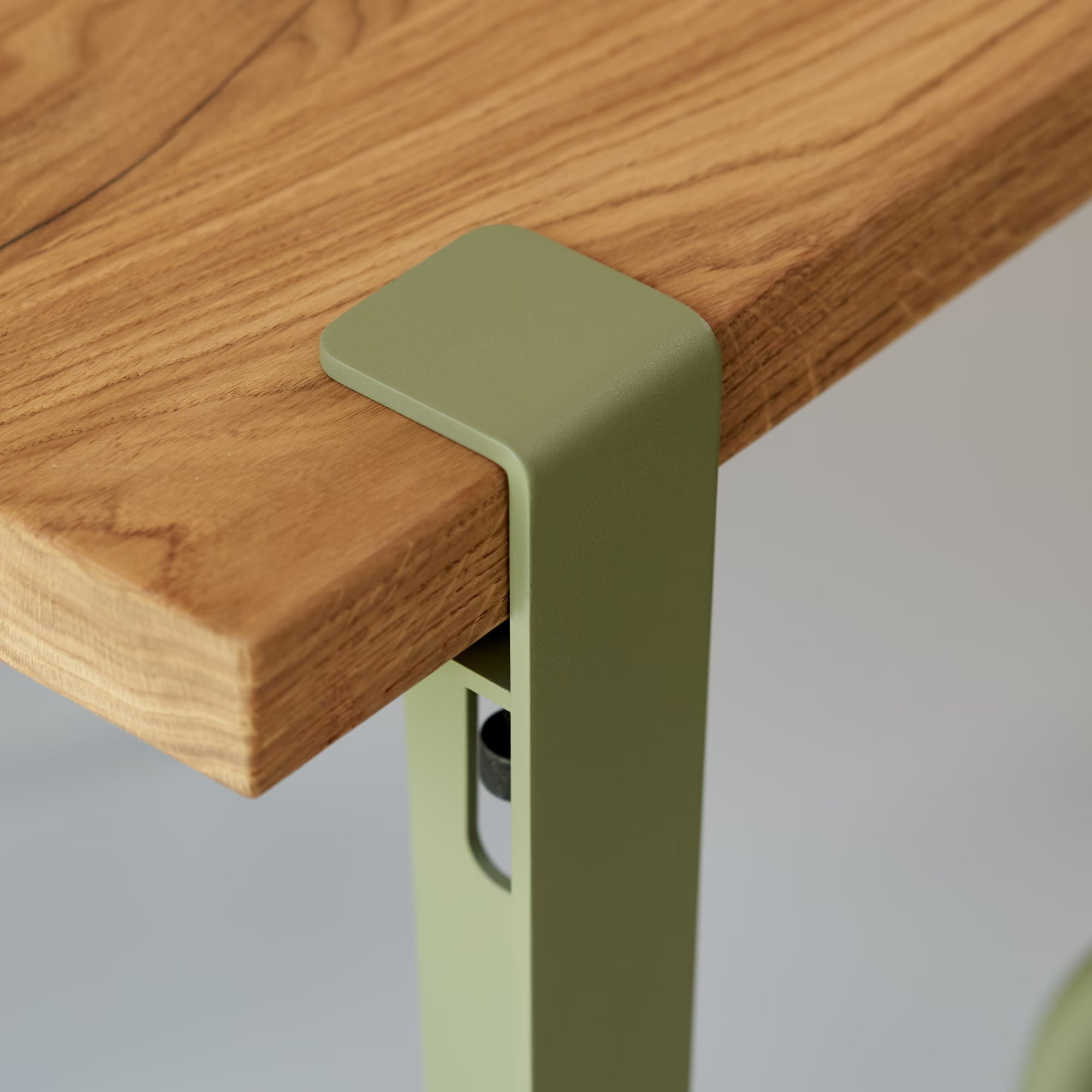 Gros plan sur plateau en bois massif et bride de fixation en métal vert kaki, vis et découpe visibles sous l’angle.