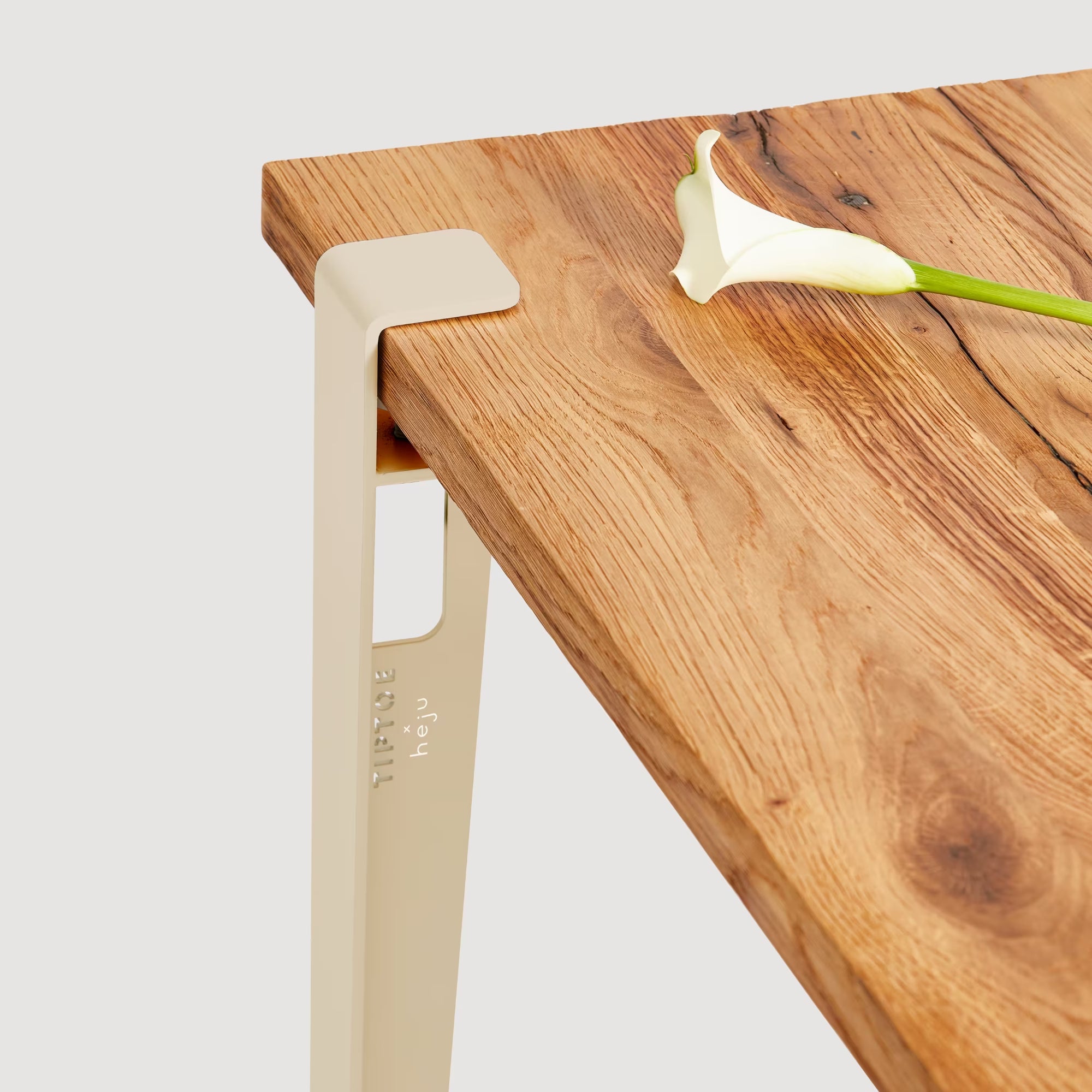 Vue rapprochée d’un pied de table beige épicéa fixé à un plateau en bois, avec une fleur blanche posée dessus.