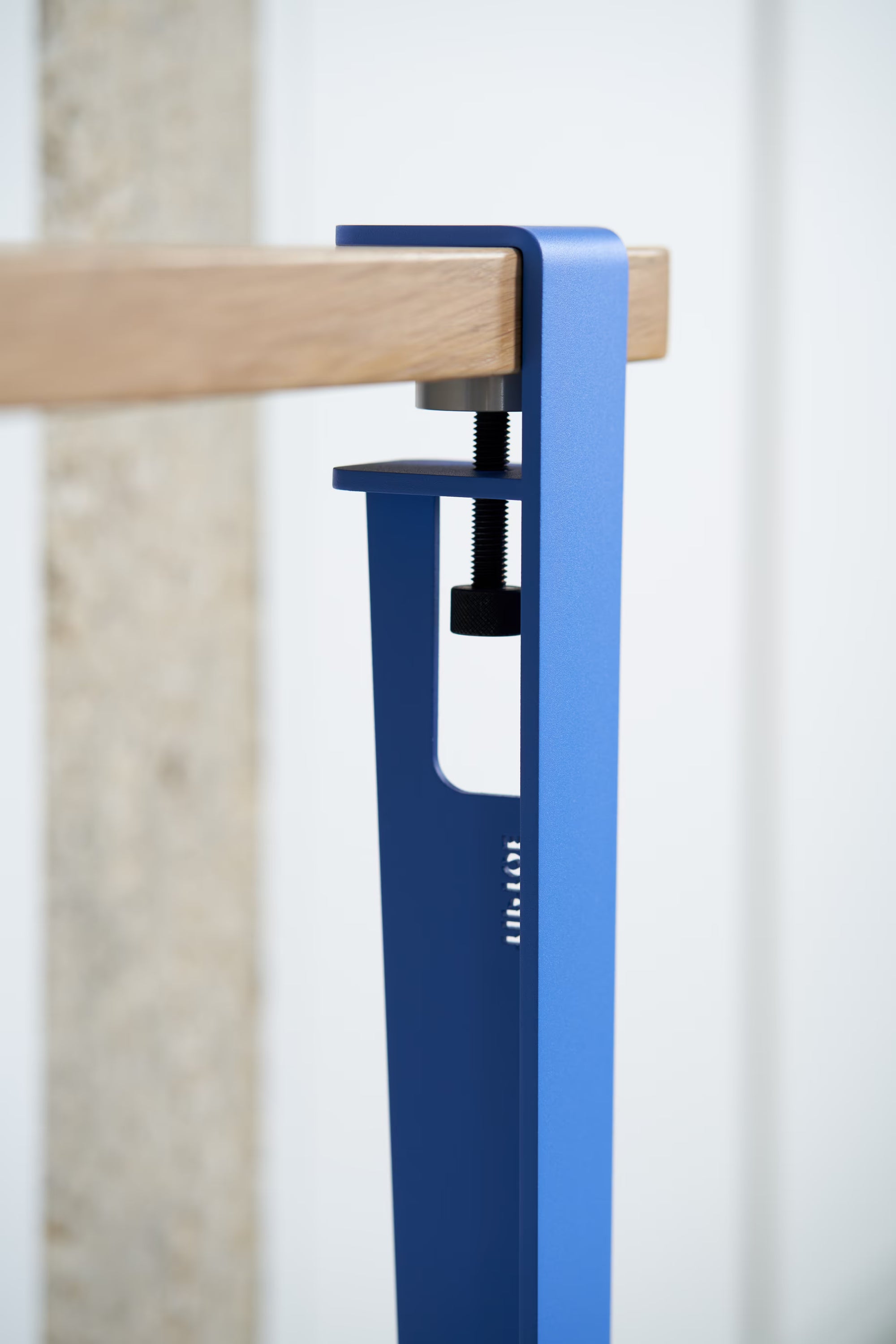 Vue rapprochée d’un pied de table bleu azur, inscription Tiptoe, fixé à un plateau en bois clair ; vis de serrage apparente.