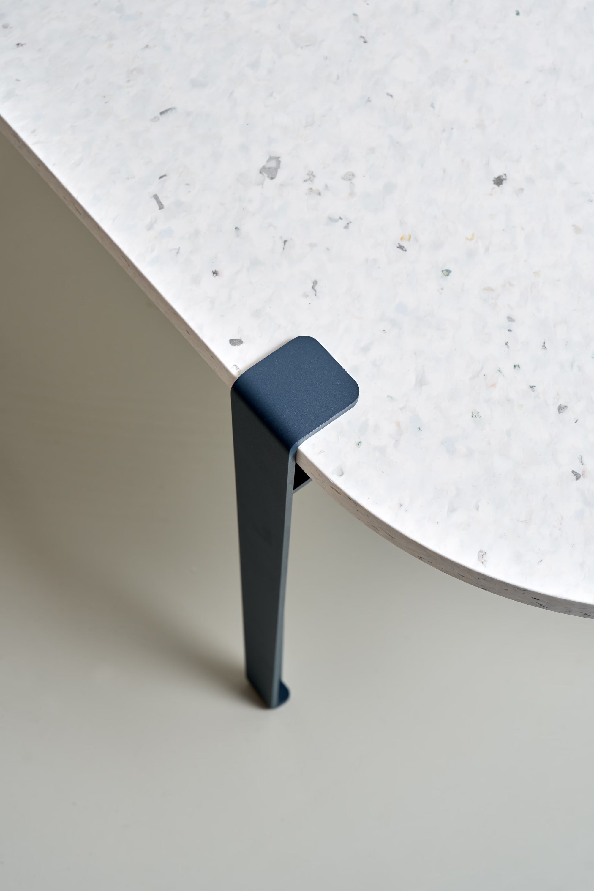 Pied de table en métal bleu nuit Tiptoe fixé à un plateau clair texturé, vue rapprochée sur l’angle.