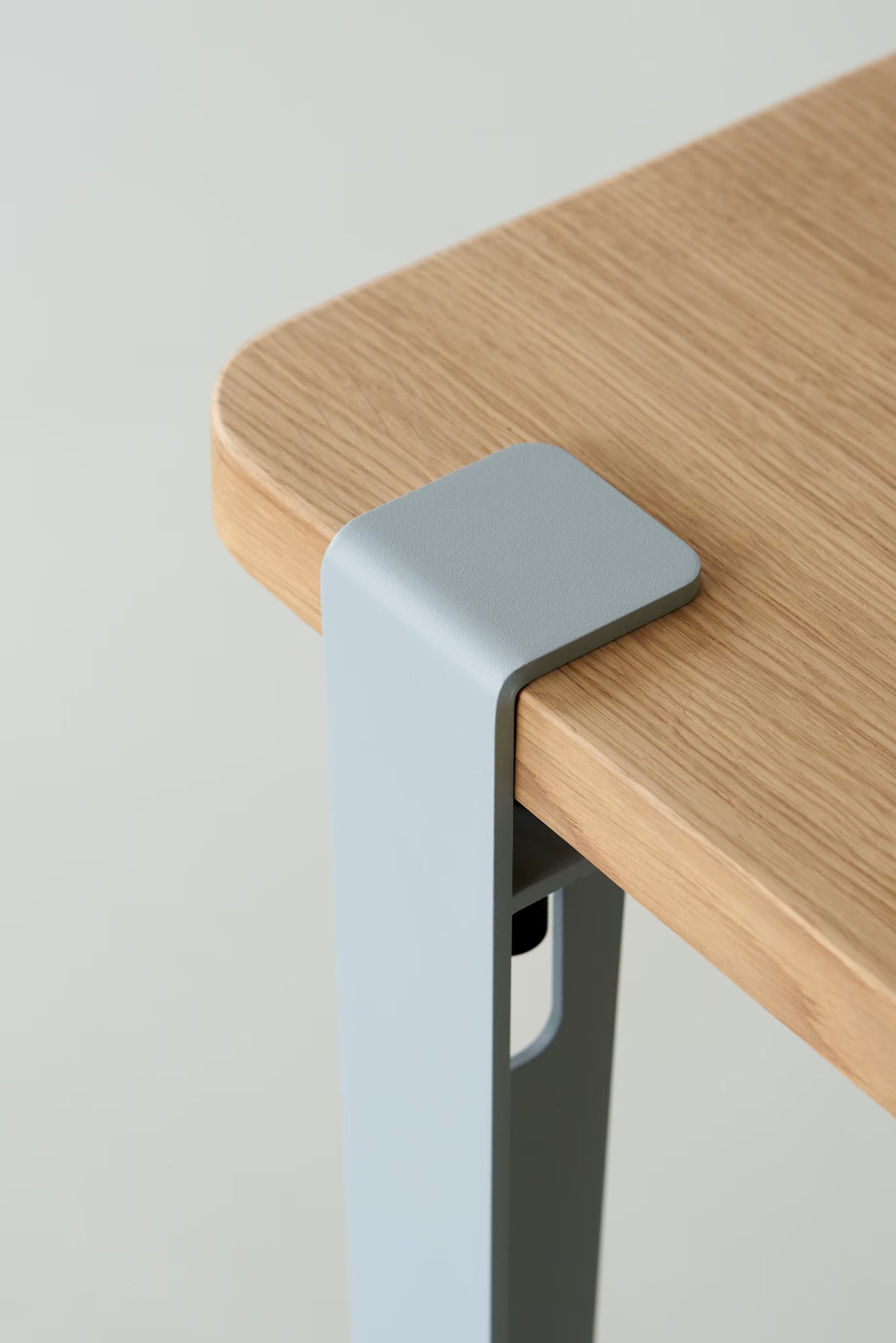 Vue rapprochée d’un pied de table en métal bleu pâle, fixé à un plateau en bois clair, avec vis de serrage apparente.
