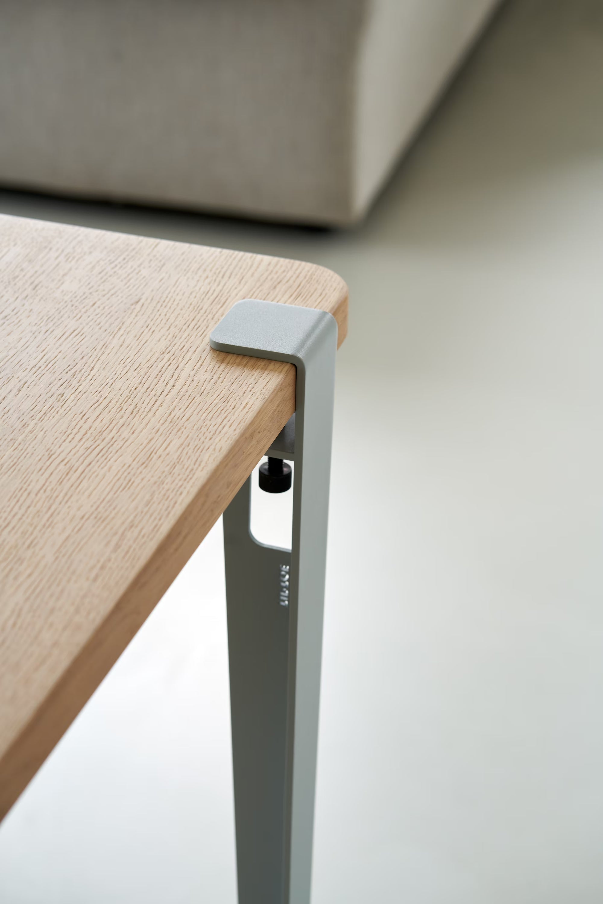 Vue rapprochée d’un pied de table en métal bleu pâle avec inscription Tiptoe, fixé à un plateau en bois, vis de serrage visible.