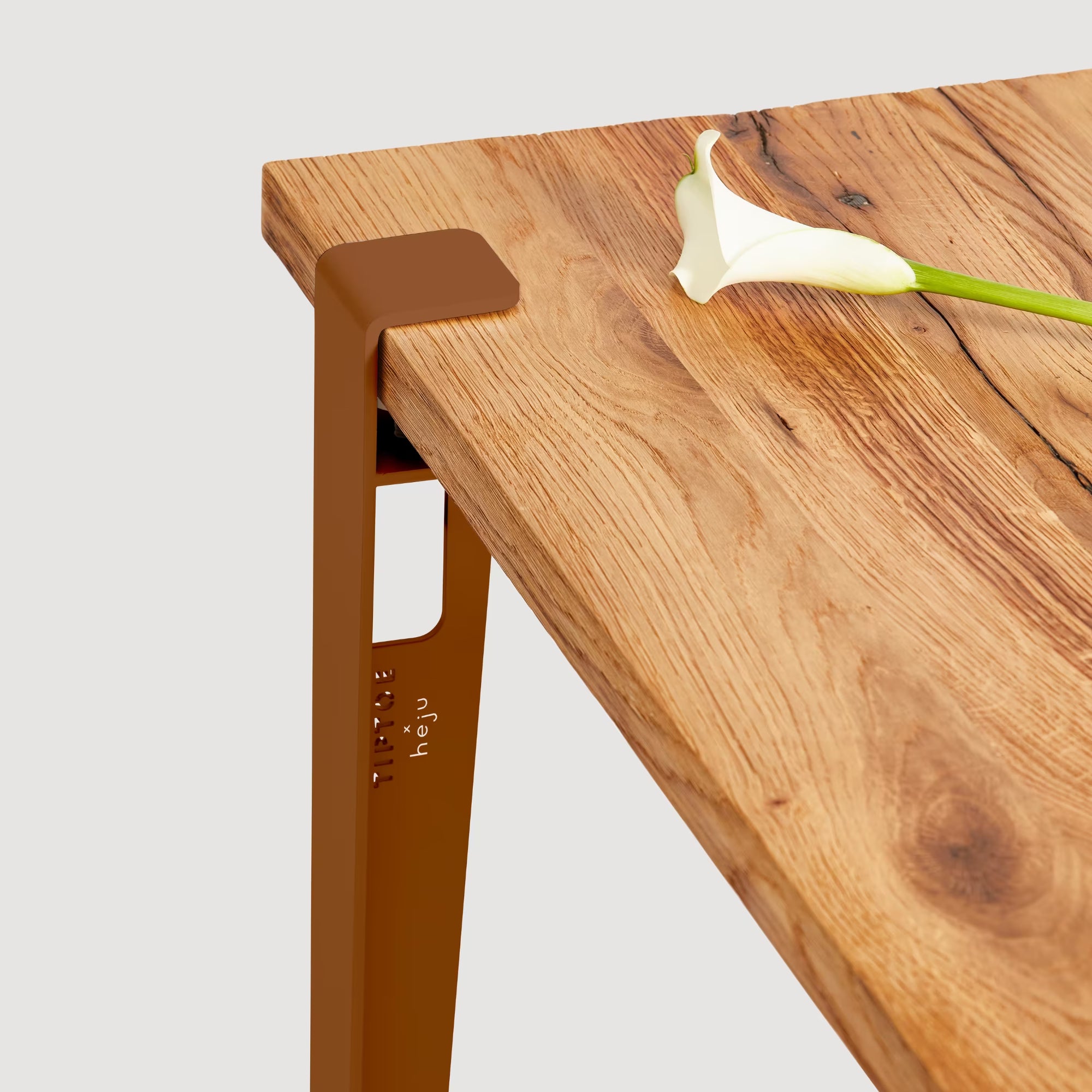 Vue rapprochée d’un pied de table brun cannelle fixé à un plateau en bois, avec une fleur blanche posée dessus.