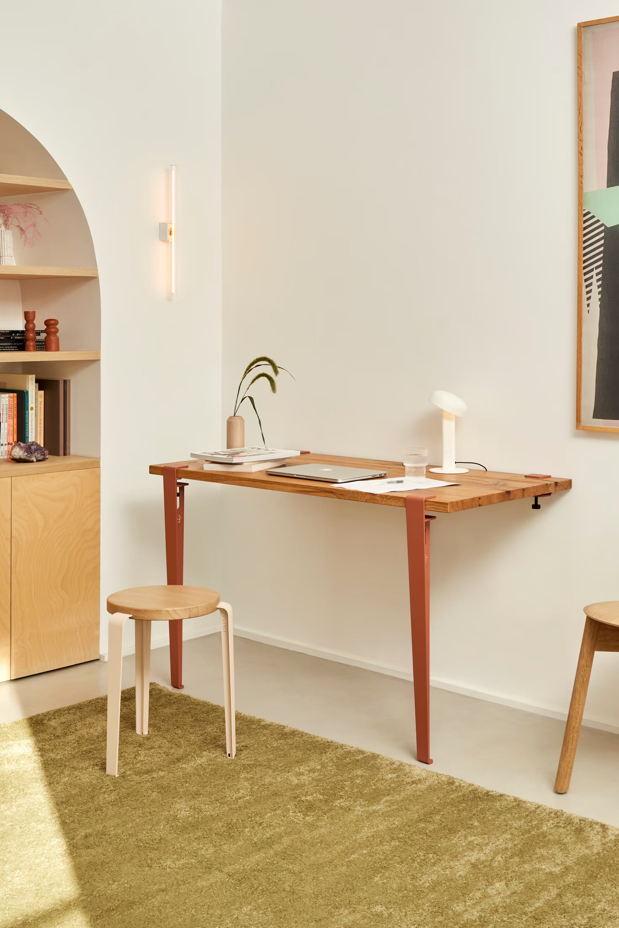 Ambiance lumineuse d’un coin bureau en bois clair, tapis olive, murs blancs, touches terracotta et lampe minimaliste.