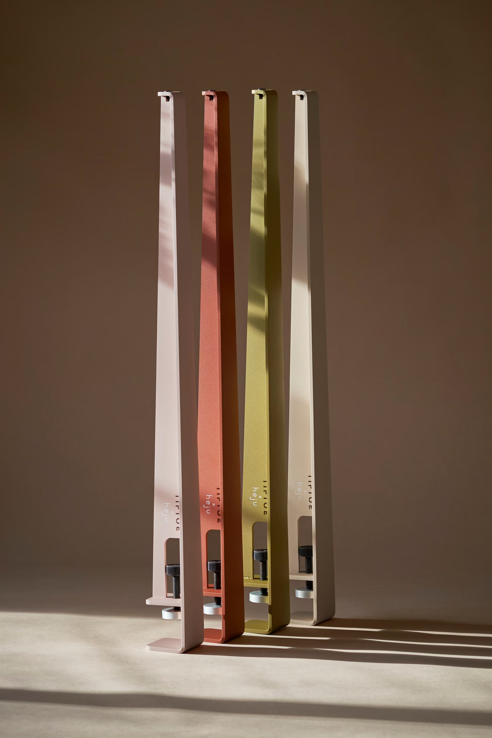 Quatre pieds de table Tiptoe debout, en rose, corail, vert et beige; logo Tiptoe et Heju visiblent en bas, éclairage studio.