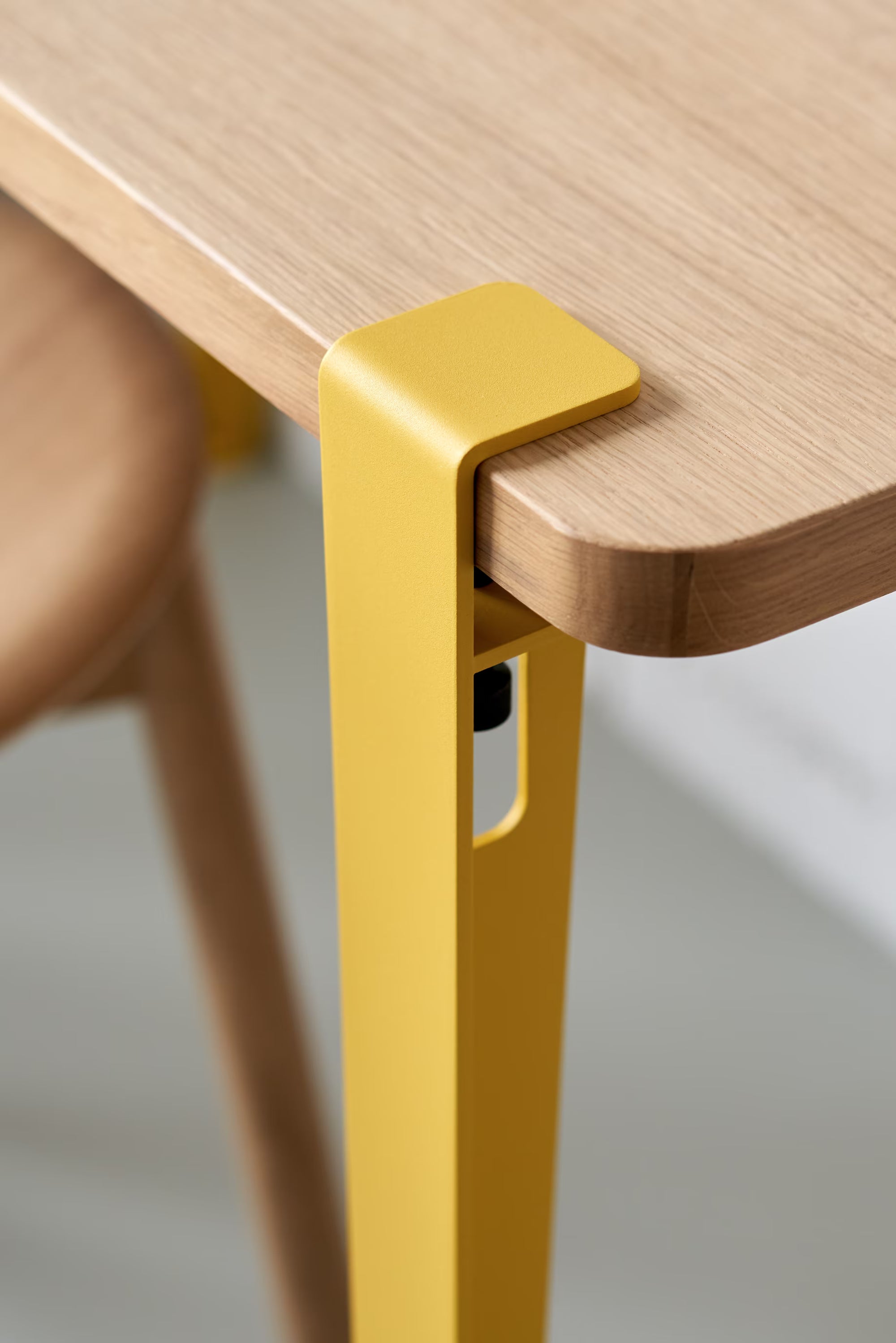 Vue rapprochée d’un pied de table jaune brioche Tiptoe fixé à un plateau en bois clair, avec vis de serrage apparente.