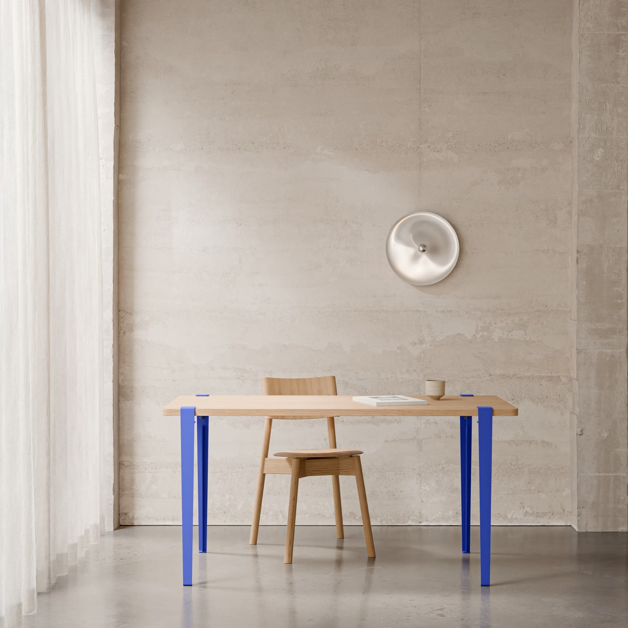 Table en bois clair avec pieds métalliques bleu Klein, accompagnée d’une chaise assortie dans un intérieur épuré.