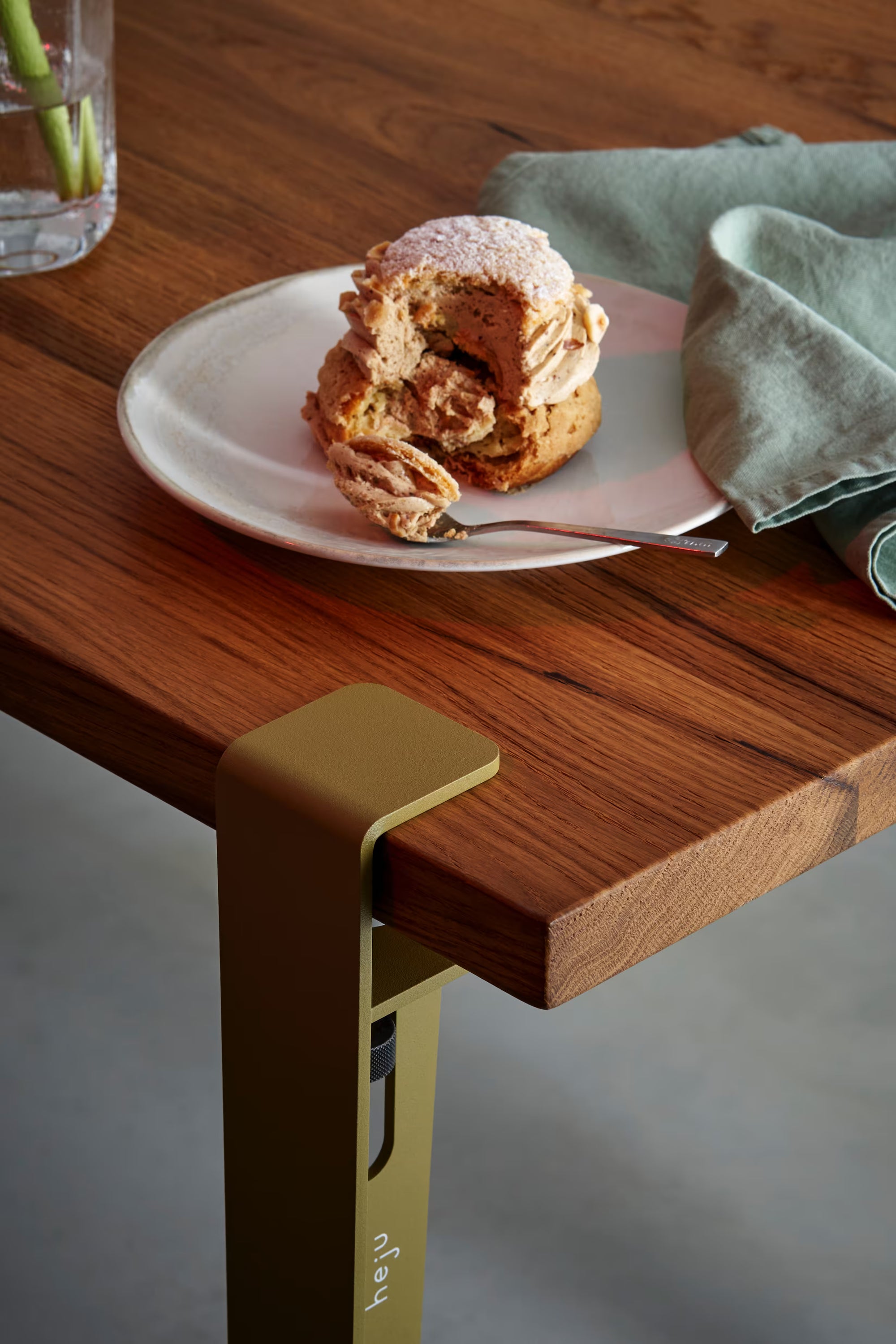 Plateau en bois avec assiette de pâtisserie et verre d’eau ; pied de table vert visible au premier plan.