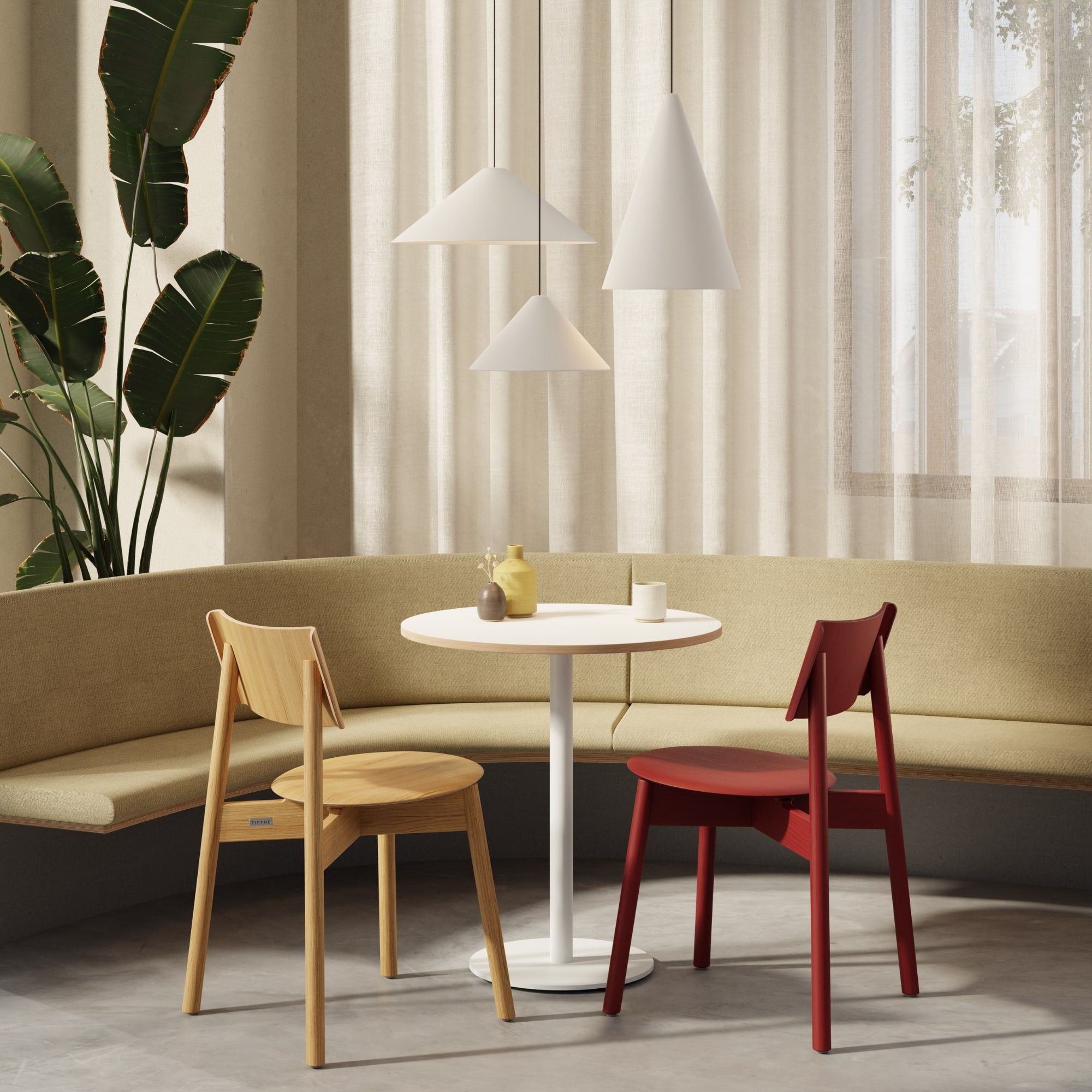 Table Moka Tiptoe blanche avec chaises SSD en bois clair et rouge, devant une banquette d’angle beige.