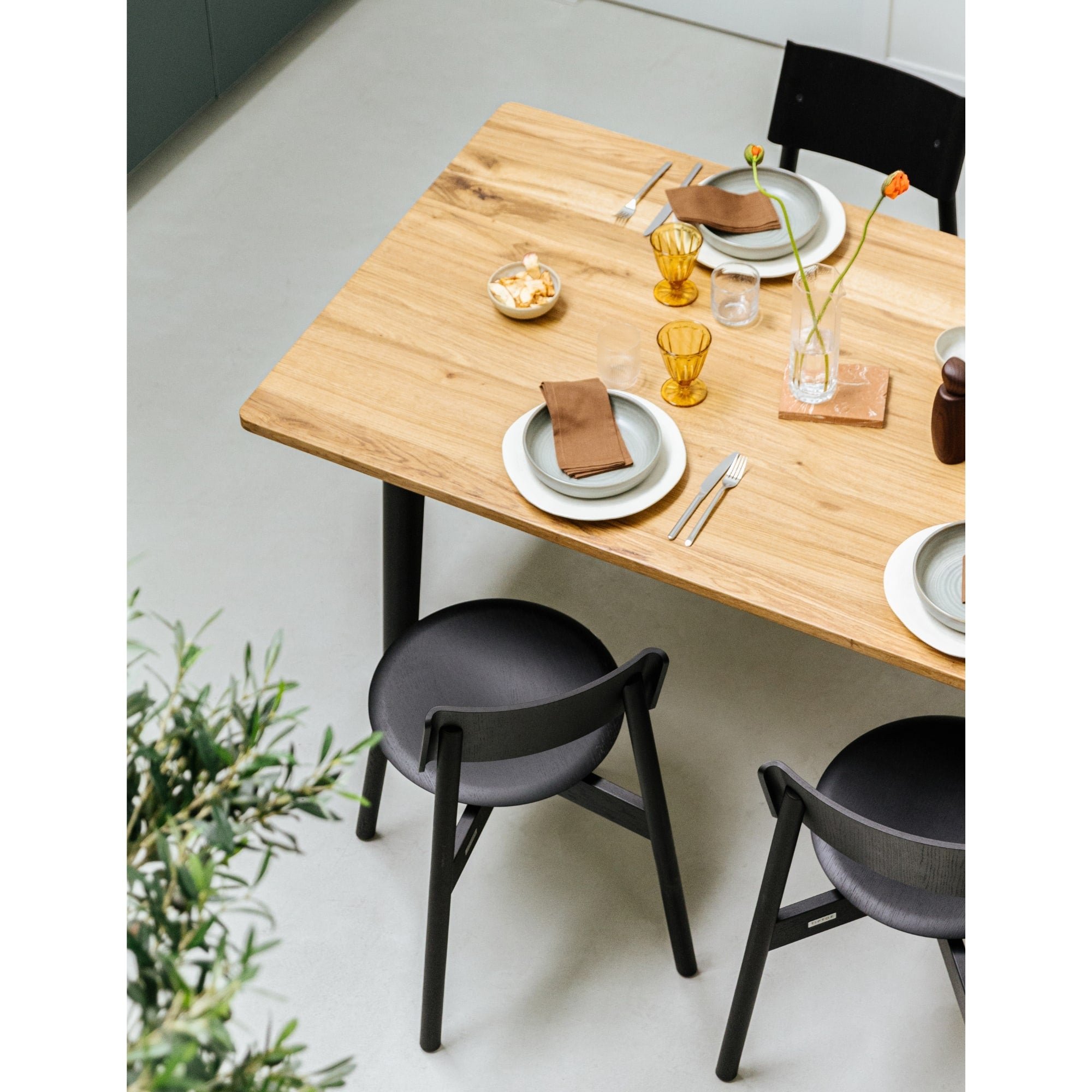 Table en bois recyclé dressée pour quatre personnes, avec vaisselle moderne et chaises noires assorties.